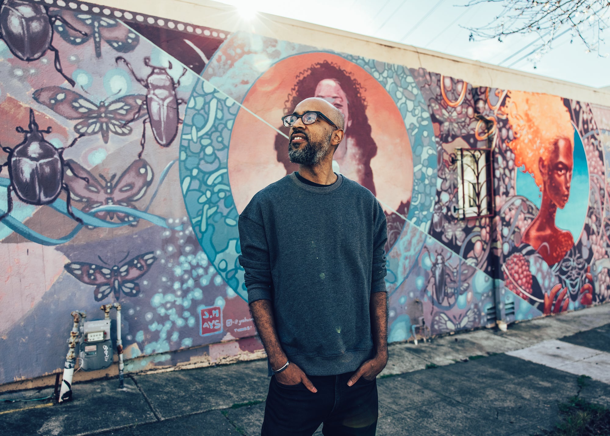 Joshua, standing and looking away, in front of one of his murals.