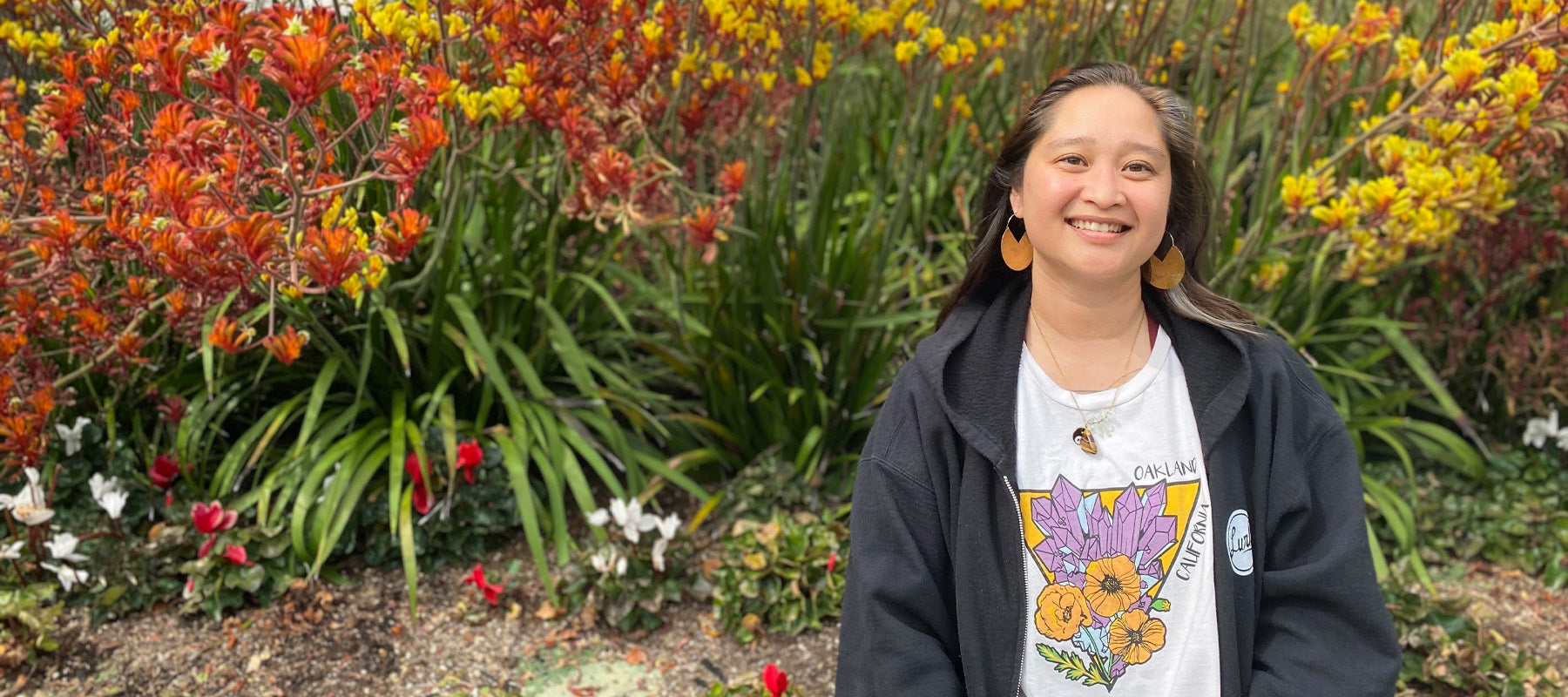 Krystal wearing Oaklandish Crystal tee outside in front of plants, smiling.