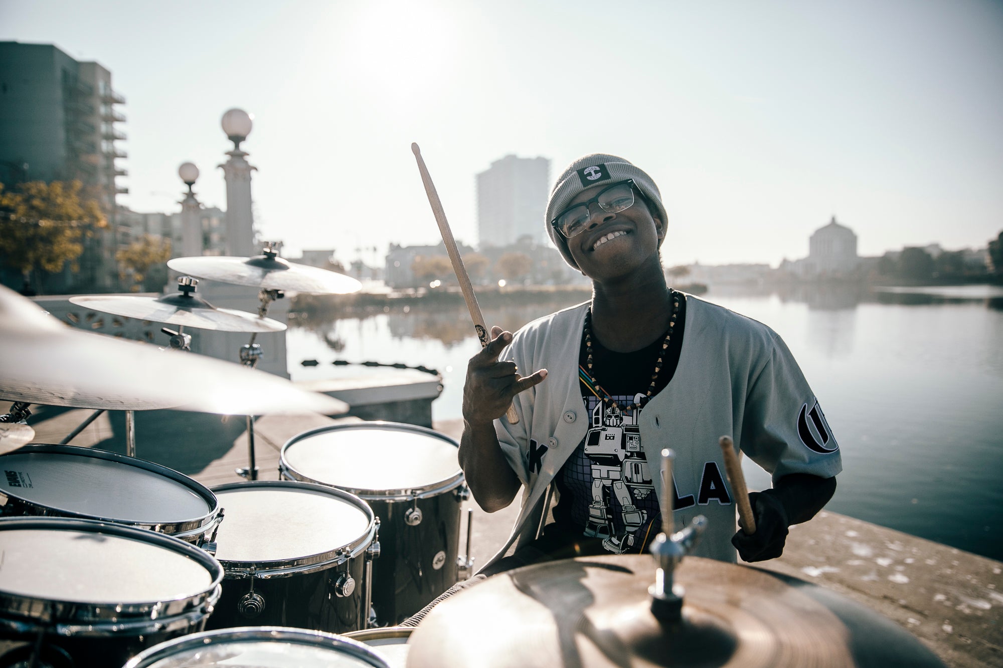 Aaron smiling, with his drum kit on the shores of Lake Merritt.