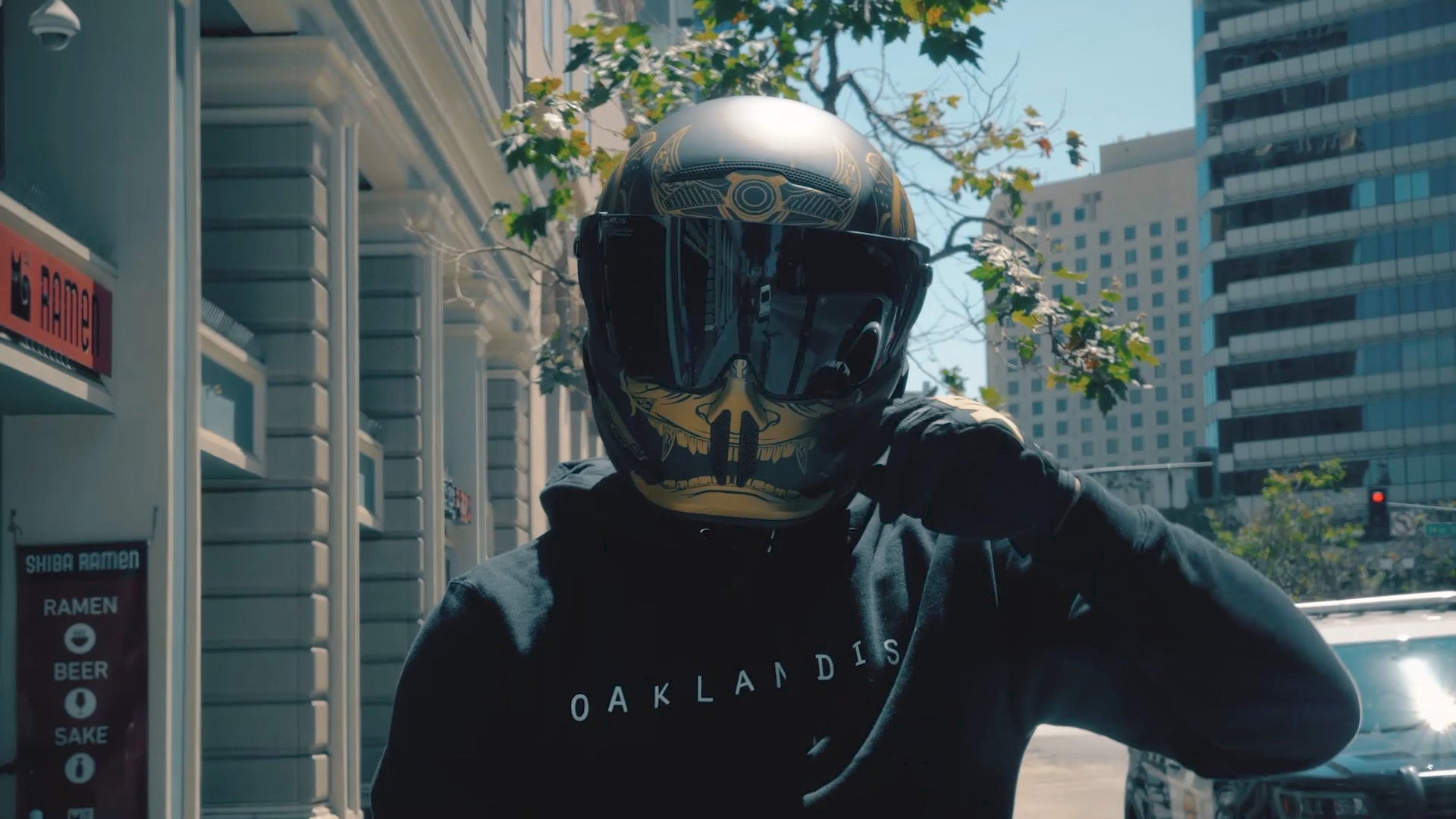 Kellen, wearing a helmet wearing black hoodie with Oaklandish text across front, on sidewalk in front of the Downtown store.