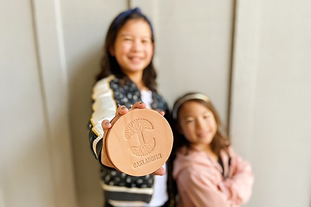 The girlsm proudly holding one of the leather custom coasters with Oaklandish logo.