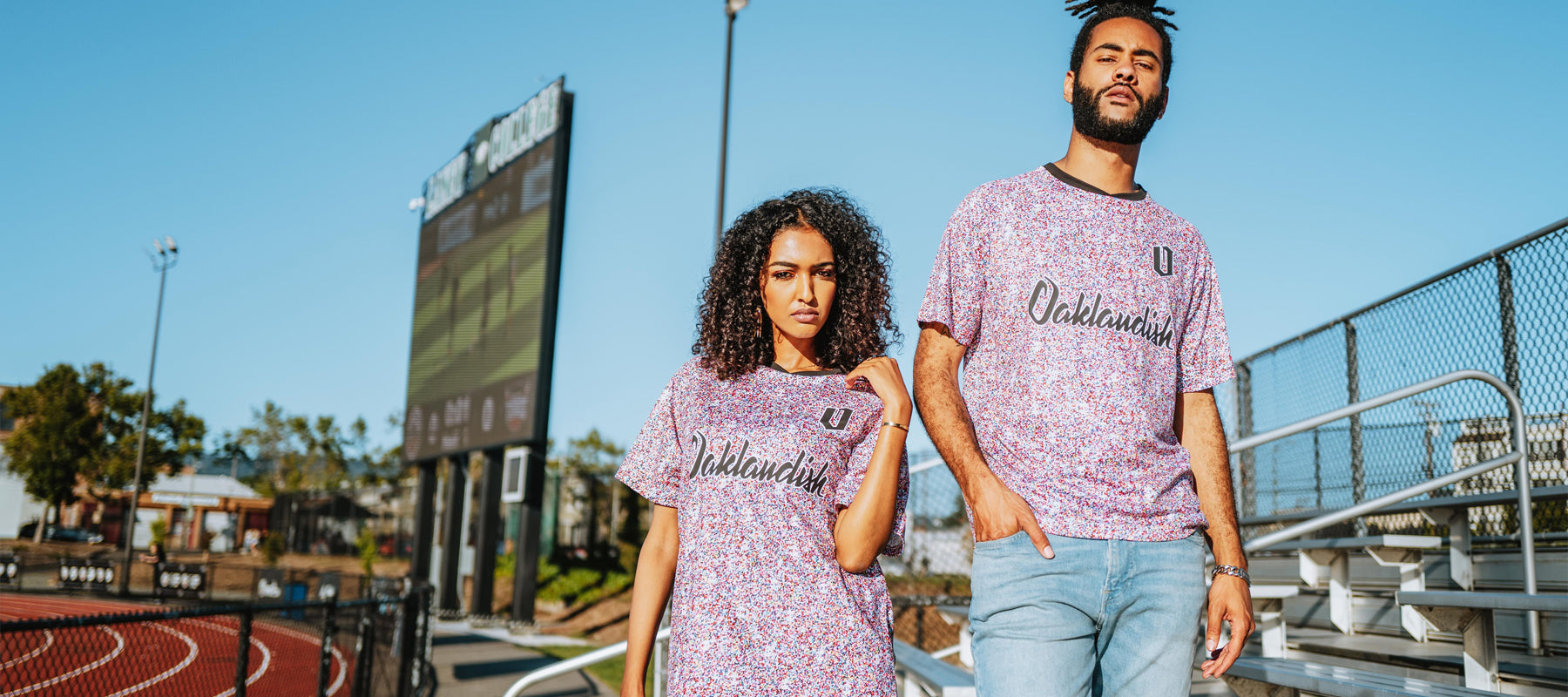 Man and women wearing multi-colored speckled soccer shirts with cursive Oaklandish wordmark and black O for Oakland applique in bleachers.