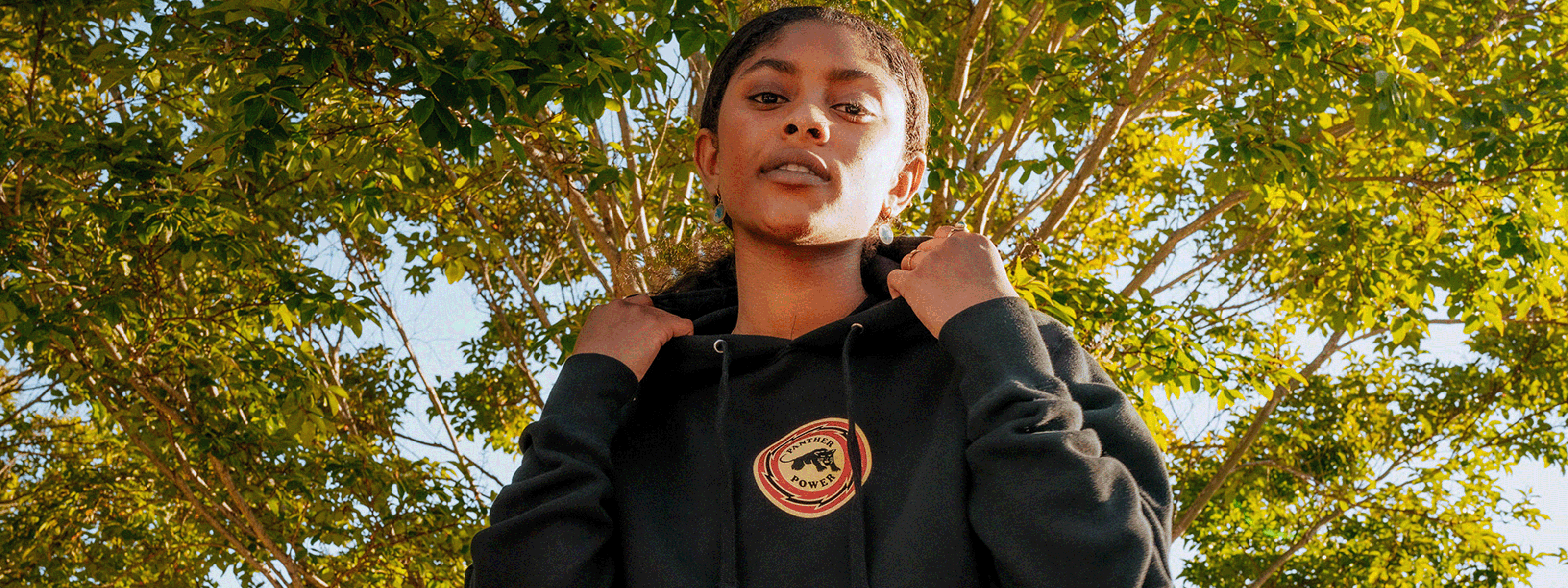 Woman wearing black pullover hoodie, under a tree.