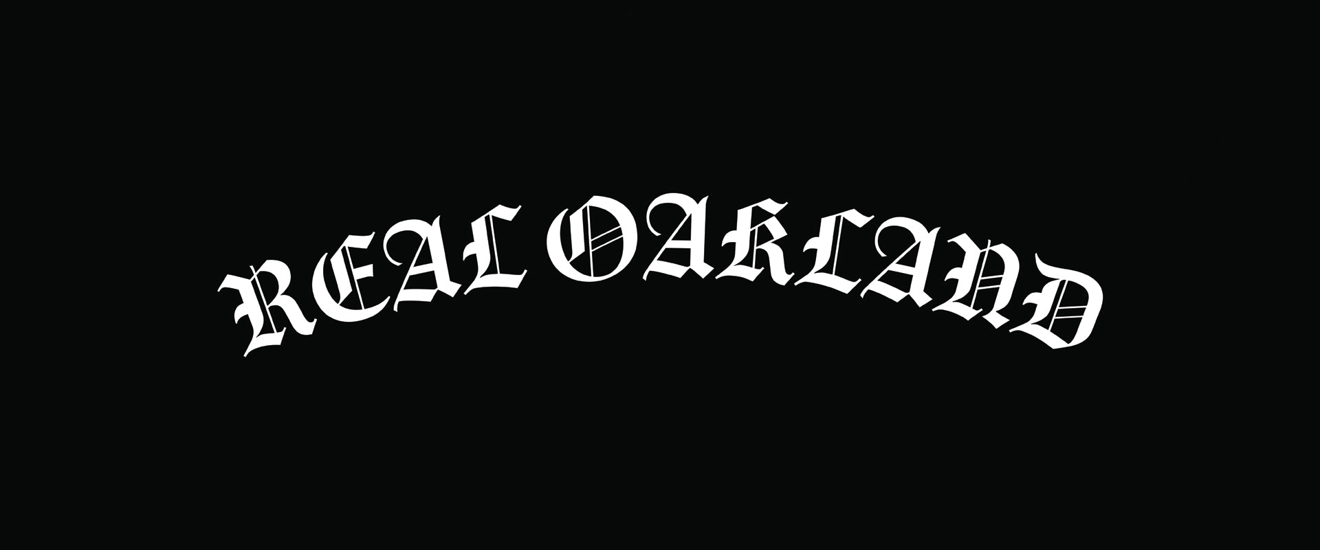 White text in a bold, curved Old English-style font reads “REAL OAKLAND” on a solid black background. The letters are ornate and outlined, giving a dramatic, classic appearance.