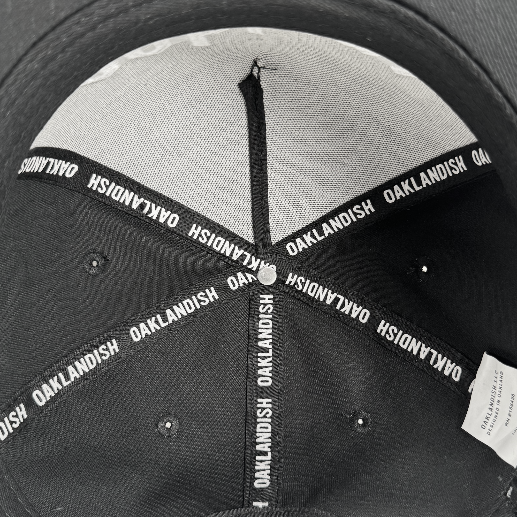 Close-up of the inside crown of the Oakland 68s Panel Cap by Oaklandish. White "OAKLANDISH" seam taping lines each panel, a white tag sits on the right, and a central metal button secures the seams.