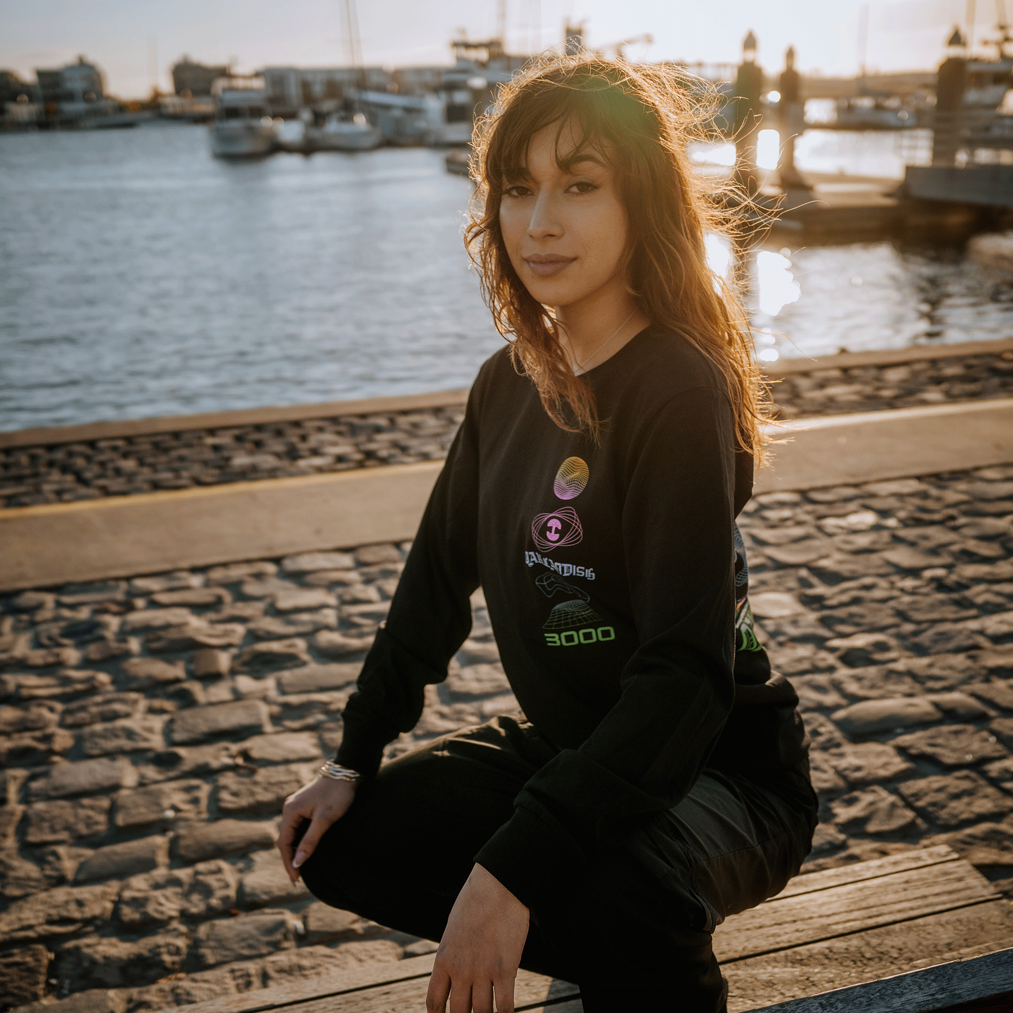 Female  model wearing long-sleeve t-shirt with neon pink, yellow, blue, and green futuristic graphic with OAKLANDISH wordmark.