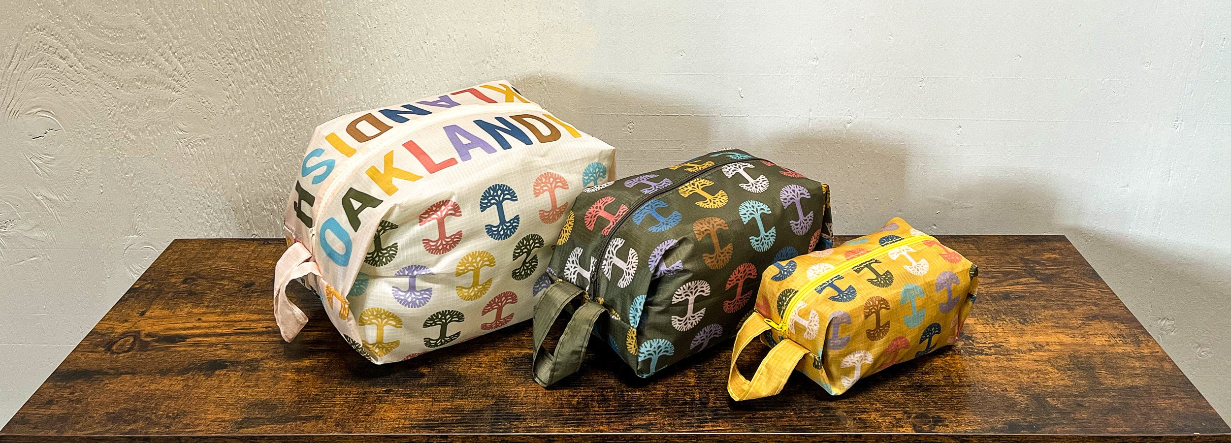 Image of three pouches, each a different color, with tree repeat pattern on wood surface.