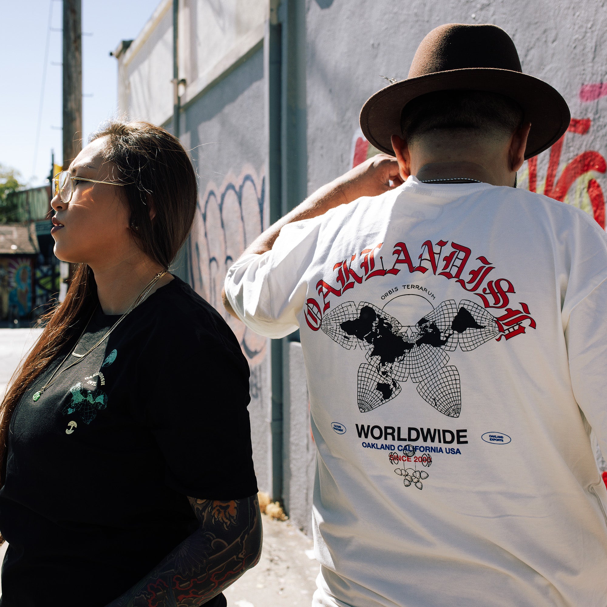 Male model showing off backside of a natural cotton color t-shirt with a large Oaklandish worldwide graphic.