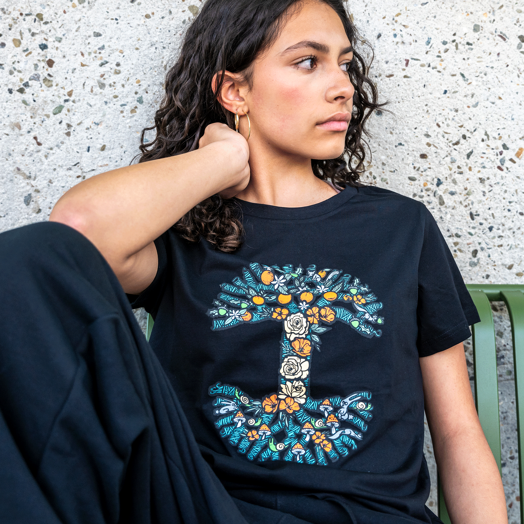 Female model wearing Women's cotton tee in black color with Oaklandish tree logo designed with nature blooming.