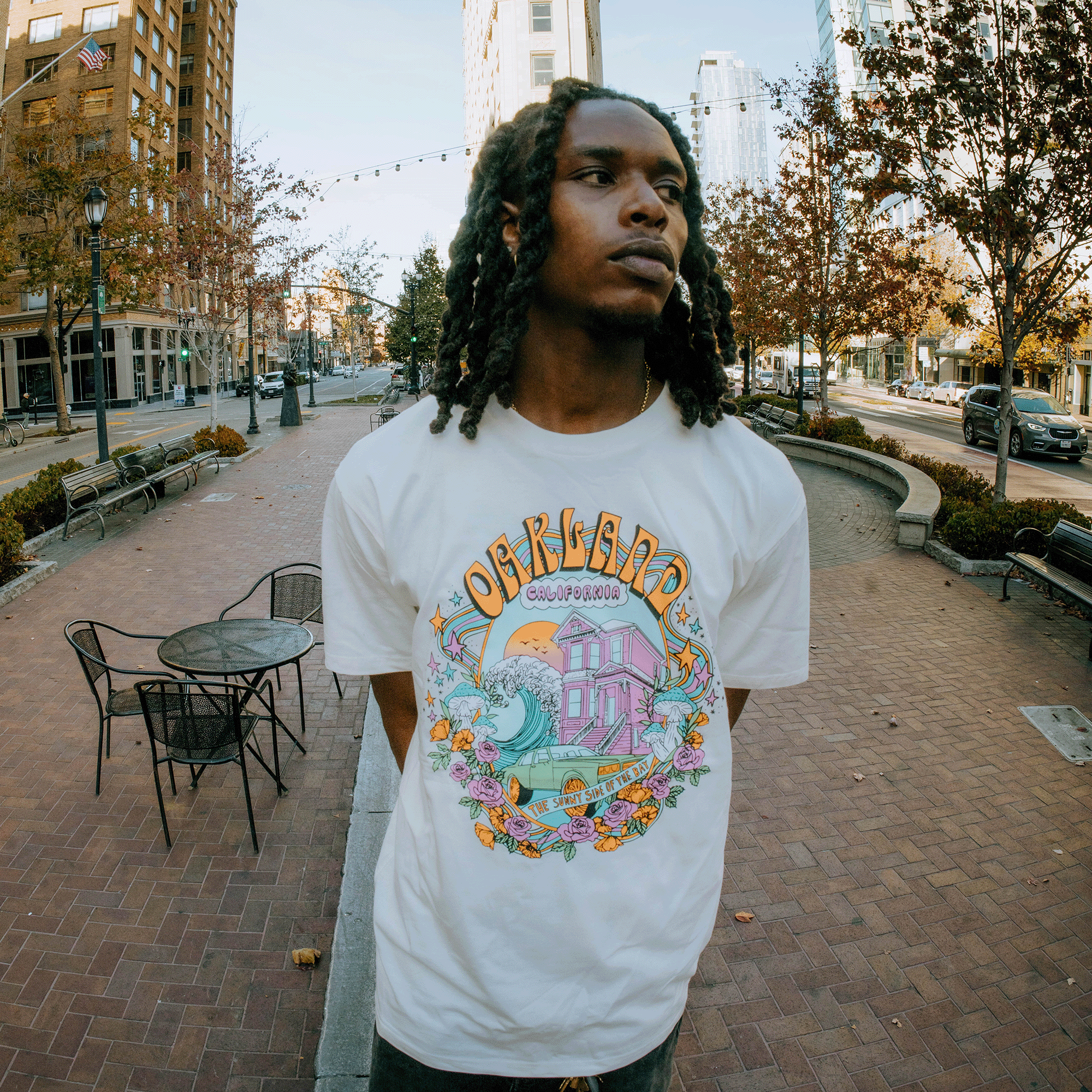 Model wearing a natural cotton colored T-shirt with a full-color dreamscape graphic with Oakland, California, Sunny Side of the Bay wordmark.