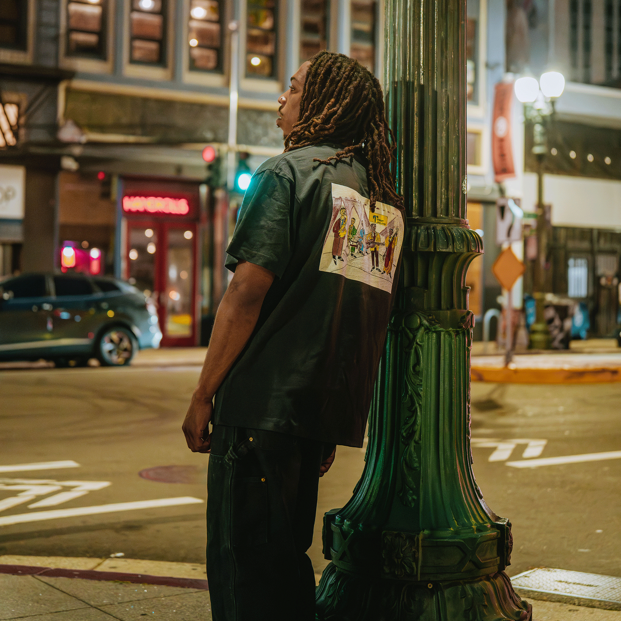 Person leaning against a green lamppost on a city street at night.