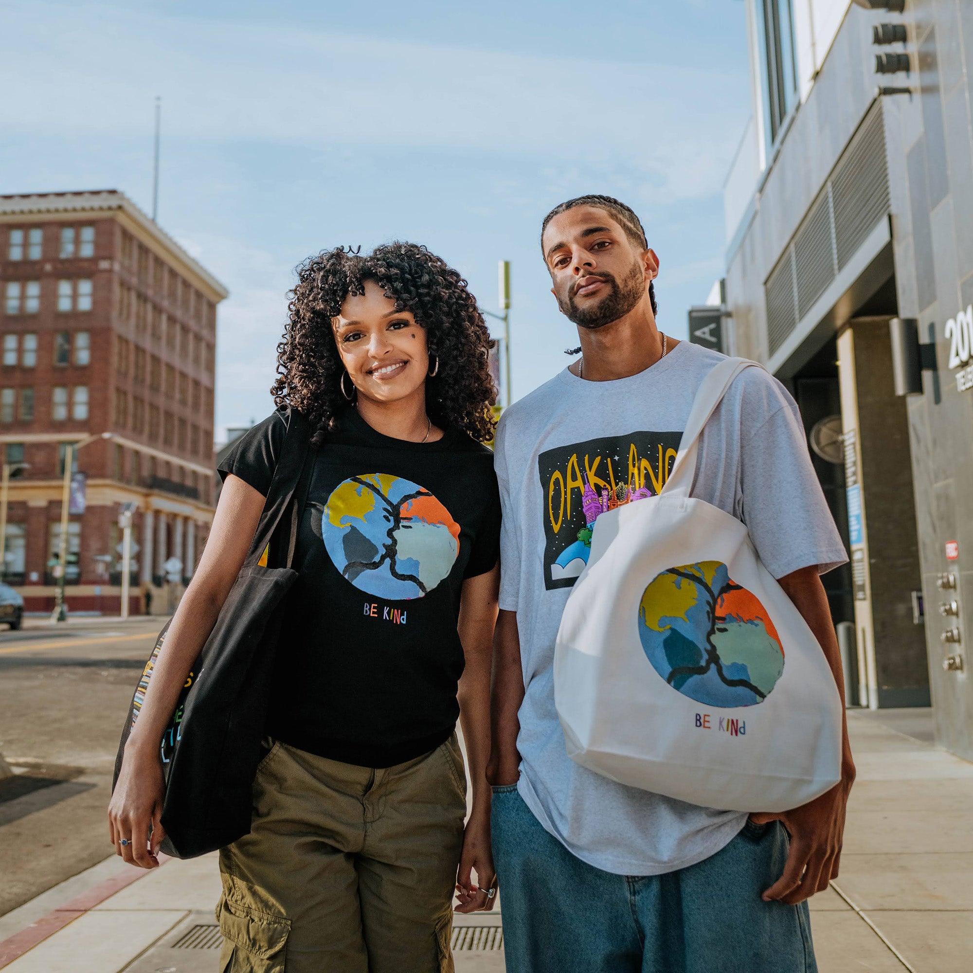 Model wearing Be Kind Oakland mural art by contemporary artist Squeak Carnwath on a cream-colored canvas tote.