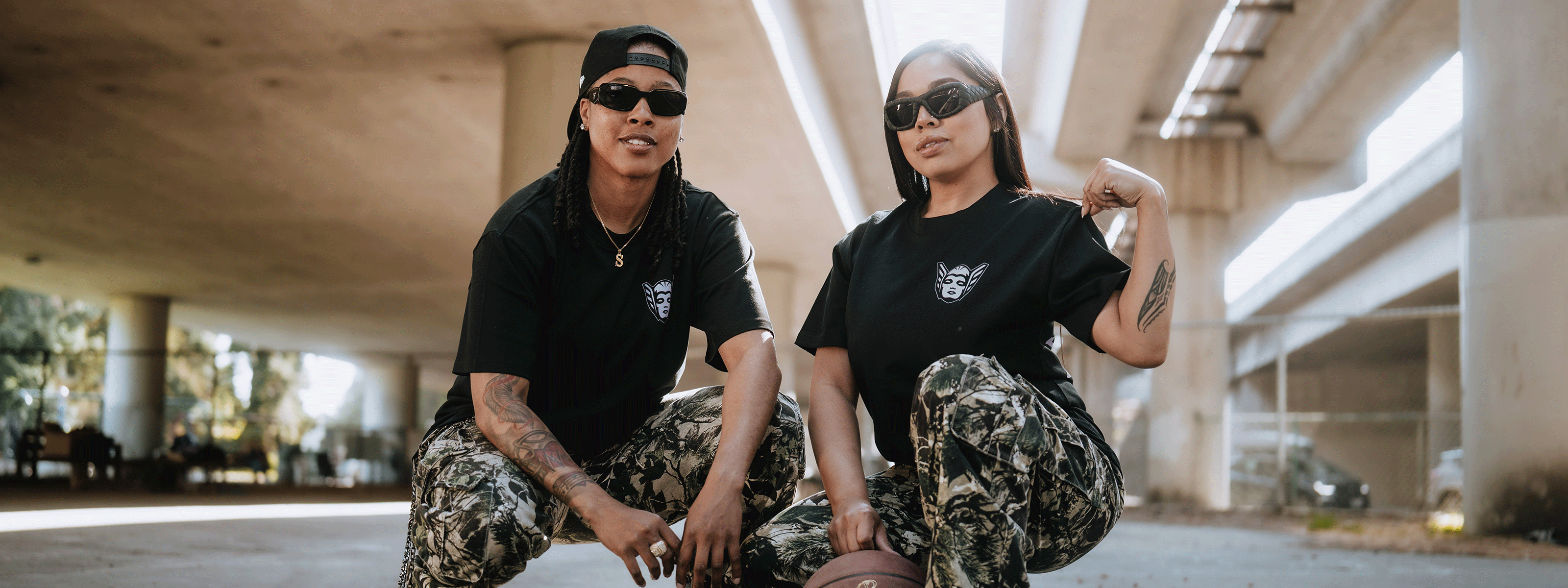 two females posed underneath freeway overpass wearing black Valkyries t-shirts