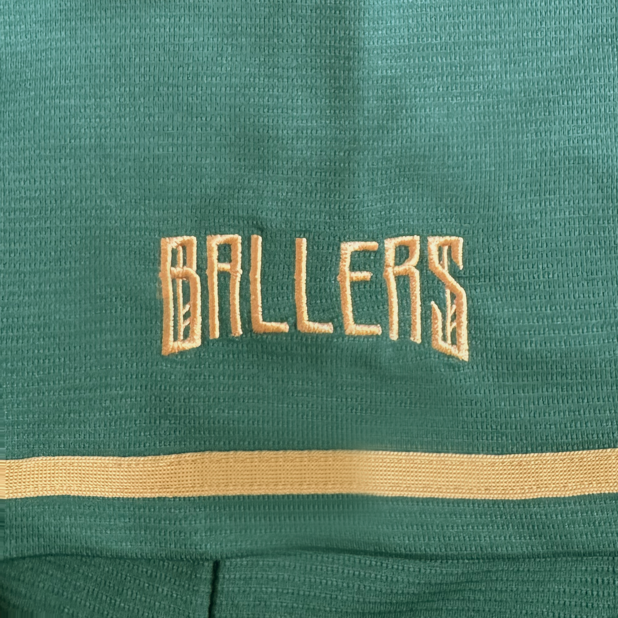 A close-up of green textured fabric from the Oakland Ballers’ Oakland Button Up Jersey, featuring “BALLERS” embroidered in beige block letters and a beige stripe below.