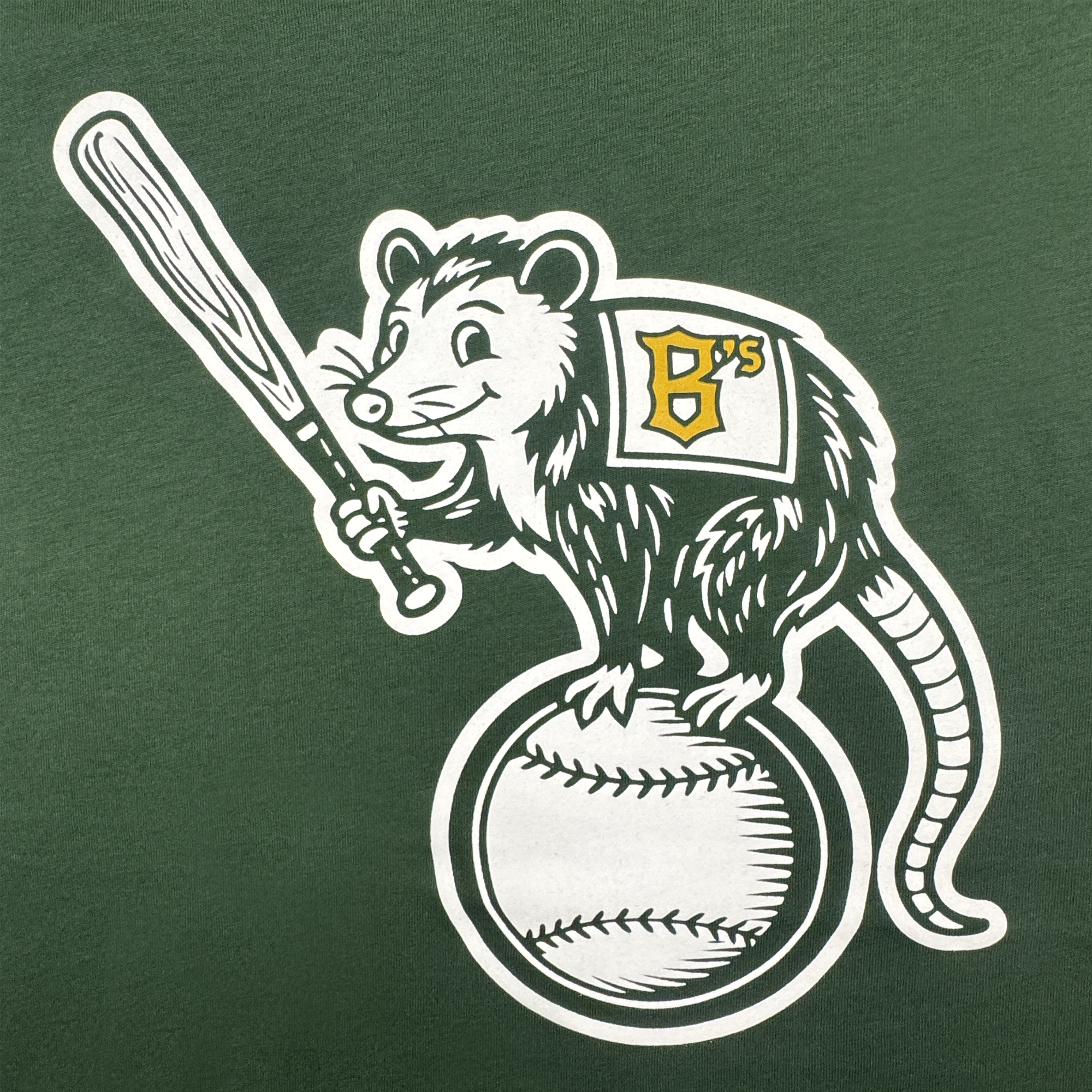 The Clutch Tee from Oakland Ballers features a cartoon opossum mascot holding a bat on a baseball, wearing a cape or jersey with a yellow "B's" logo—stands out on green, perfect for any pro baseball fan!.