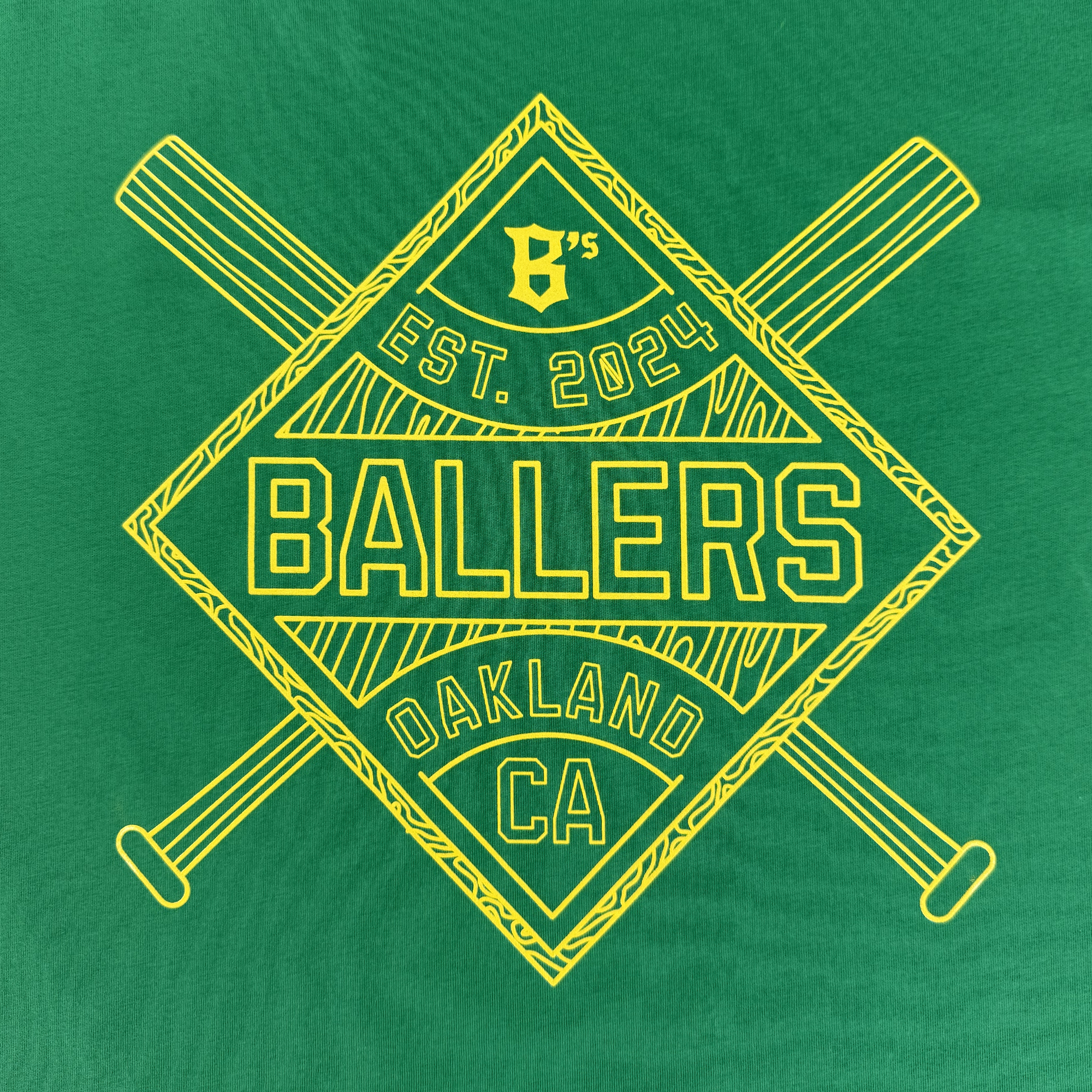 The Classic Diamond Tee by Oakland Ballers features a green background with a yellow diamond logo, crossed bats, and "B’s EST. 2024 BALLERS OAKLAND CA" text—a perfect Pro Baseball Team style for Oakland fans.