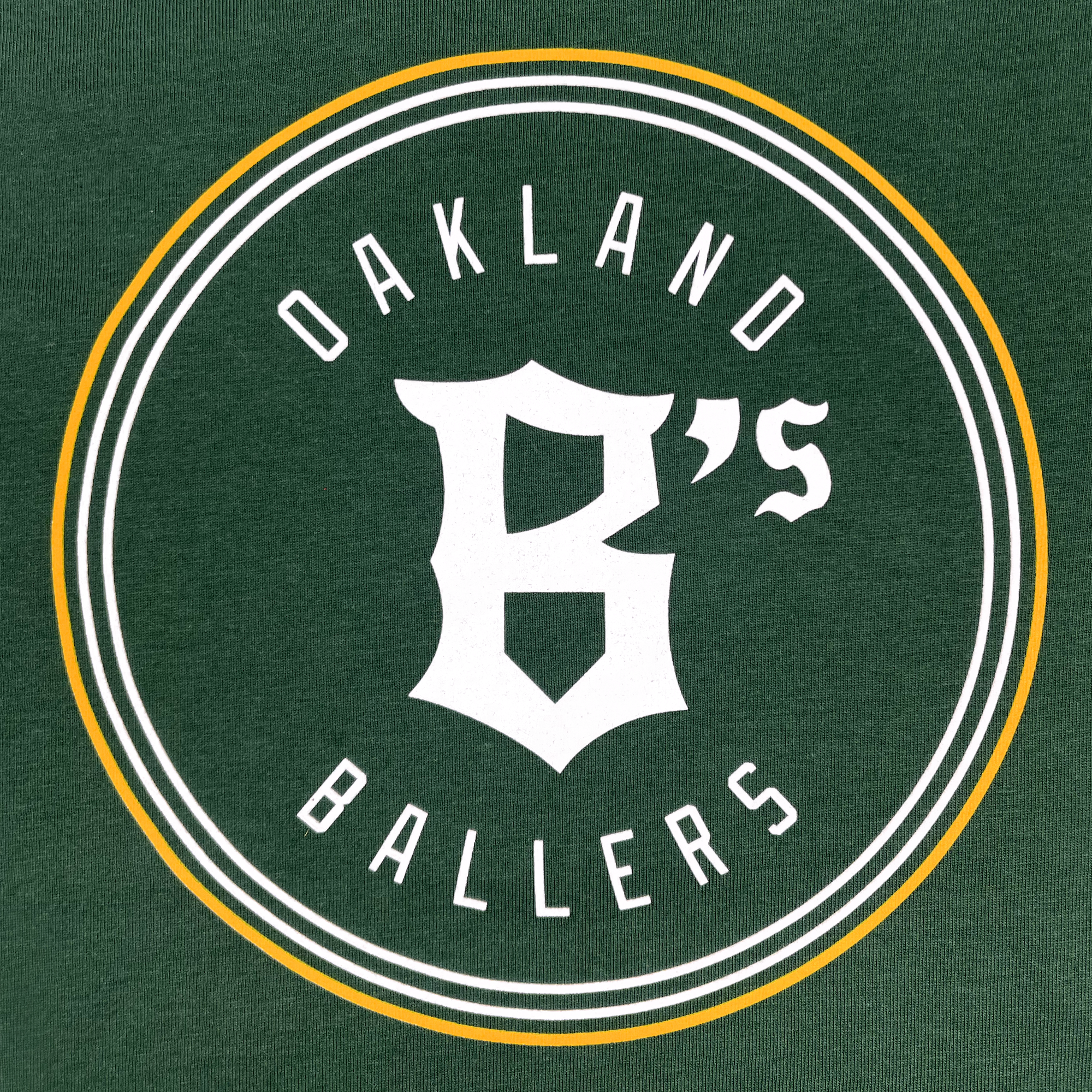 Detailed front of baby one-piece in forest green with yellow and white Oakland Ballers logo centered .