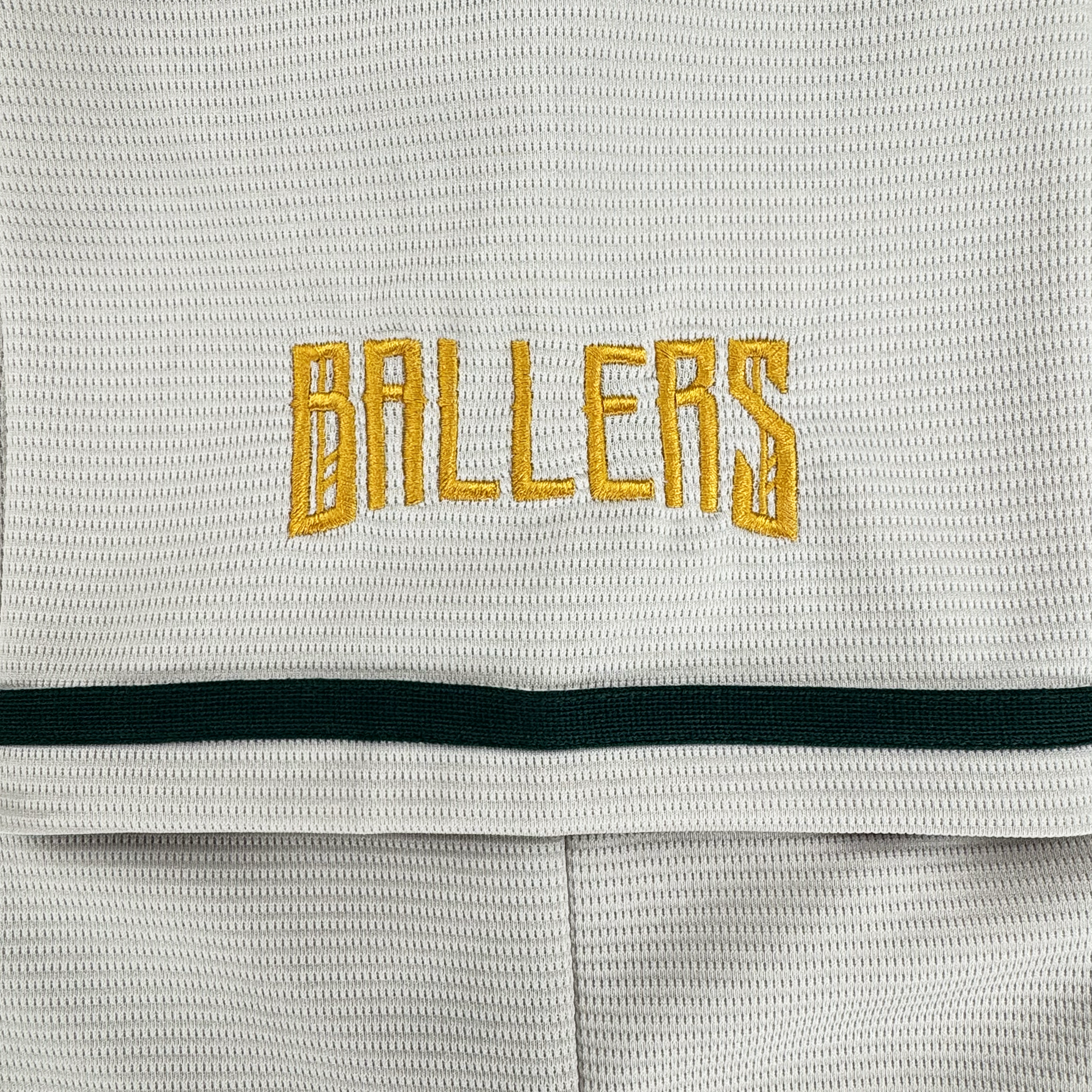 A close-up of the Oakland Ballers Button Up Jersey by Oakland Ballers shows white textured fabric with "BALLERS" in yellow block embroidery and a dark green stripe across the lower section.