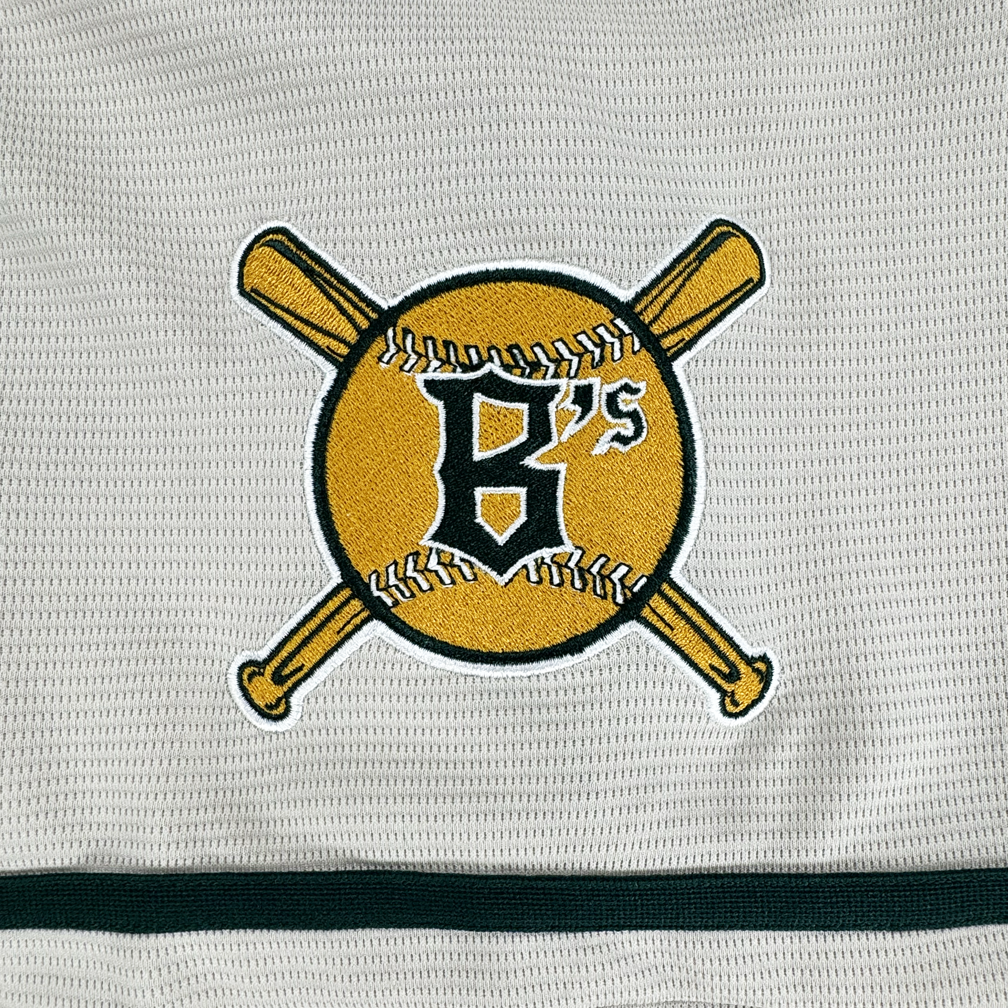 The Oakland Ballers Button Up Jersey features an embroidered yellow baseball patch with white stitches, a black "B’s," and crossed bats—showcasing the Oakland Ballers brand on textured white fabric with a black stripe.
