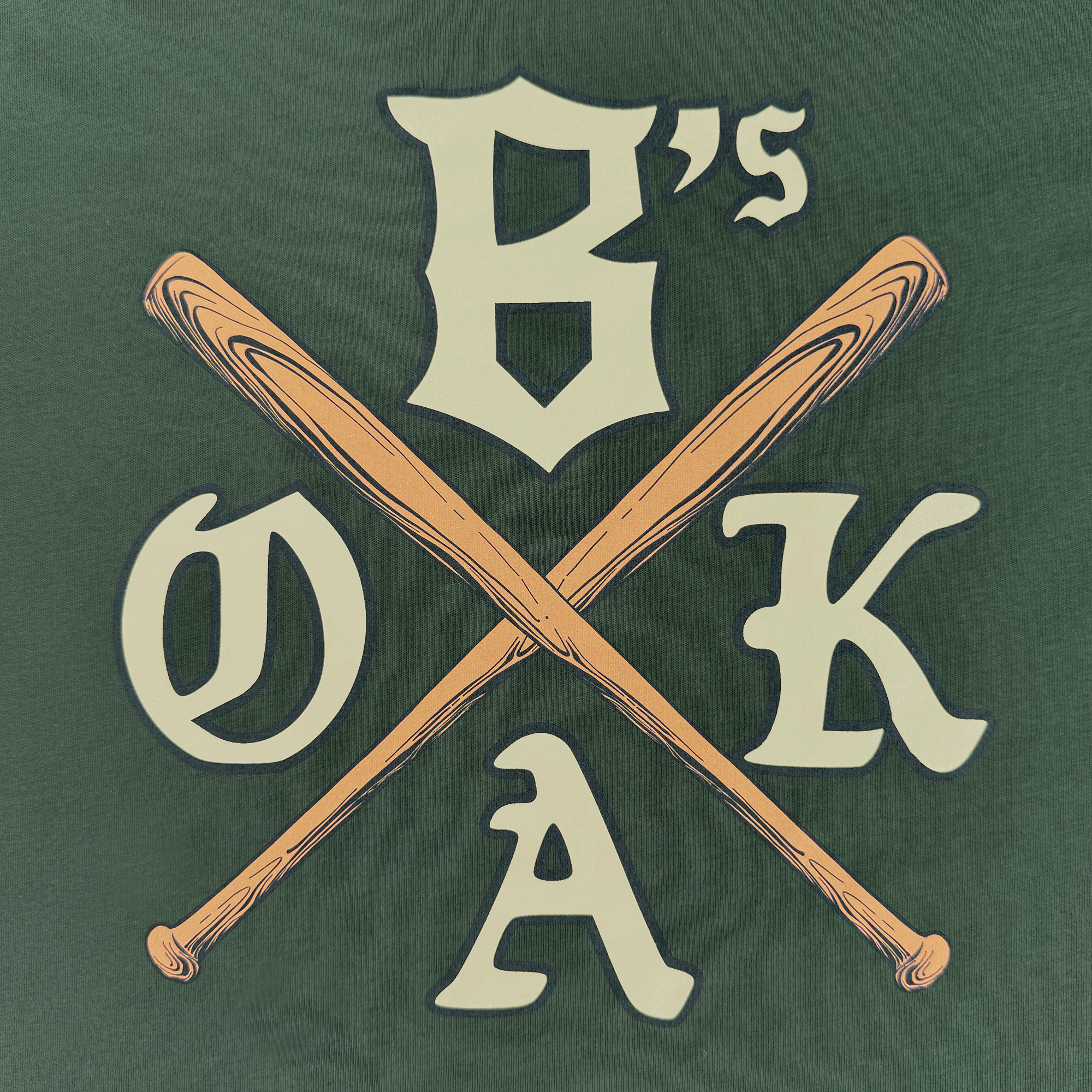 The OAK Bat Tee by Oakland Ballers features two crossed tan bats on a dark green background with large cream "O," "K," "A," and a stylized "B’s" in classic fit t-shirt style, representing the Oakland Ballers Pro Baseball Team.