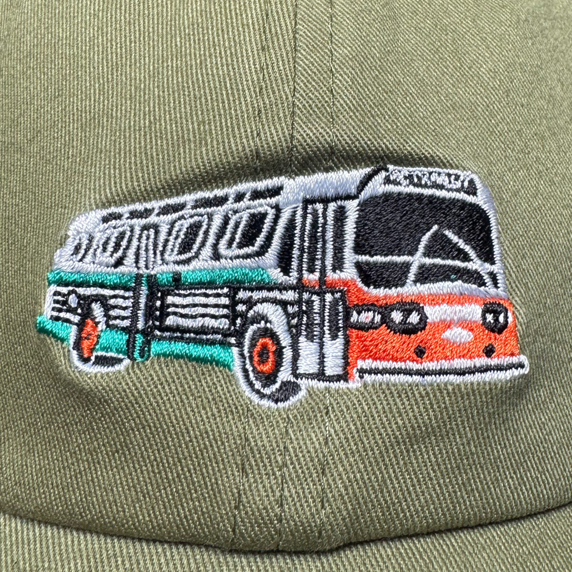 Oaklandish AC Transit Dad Hat features an embroidered patch of a vintage bus in silver, black, orange, and teal on olive fabric, with “MUNI” above the windshield and classic vintage details like large windows and detailed lines.