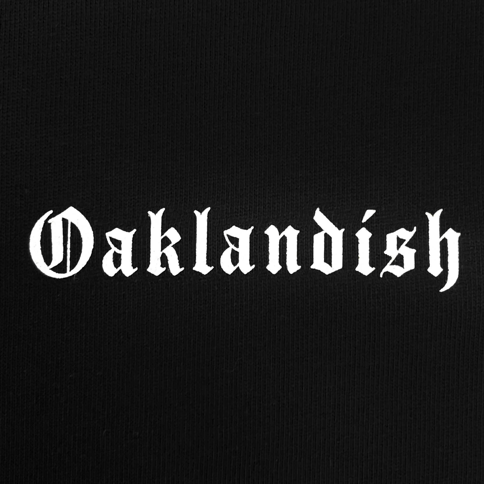 Detailed close-up of white OAKLANDISH wordmark in trip on a black baseball jersey.