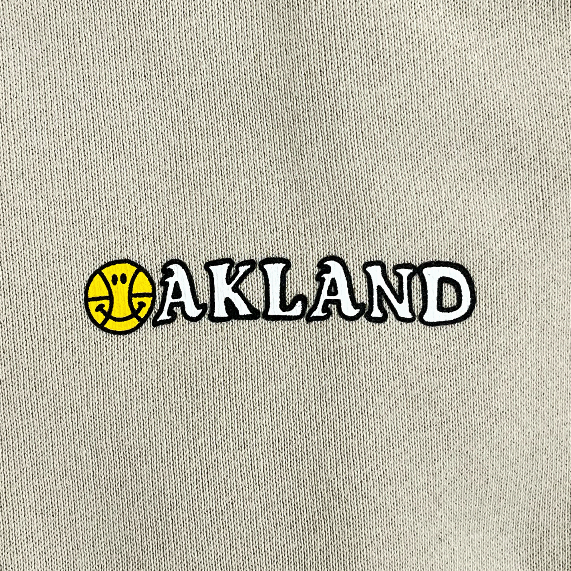 Close-up of OAKLAND wordmark with yellow basketball ball as the O on an ivory pullover hoodie sweatshirt. 