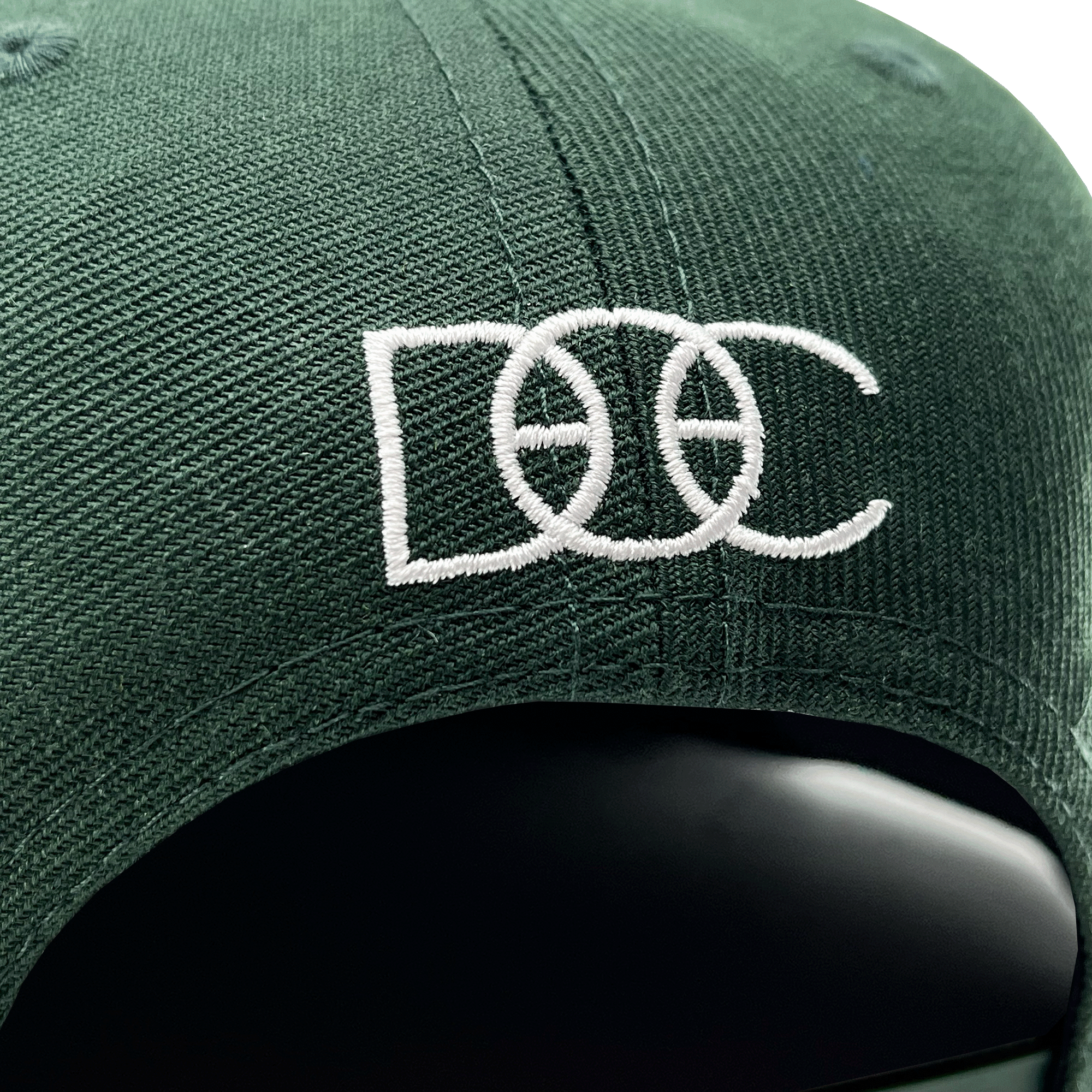 Close-up of the white embroidered DOC wordmark on the back of a green cap.