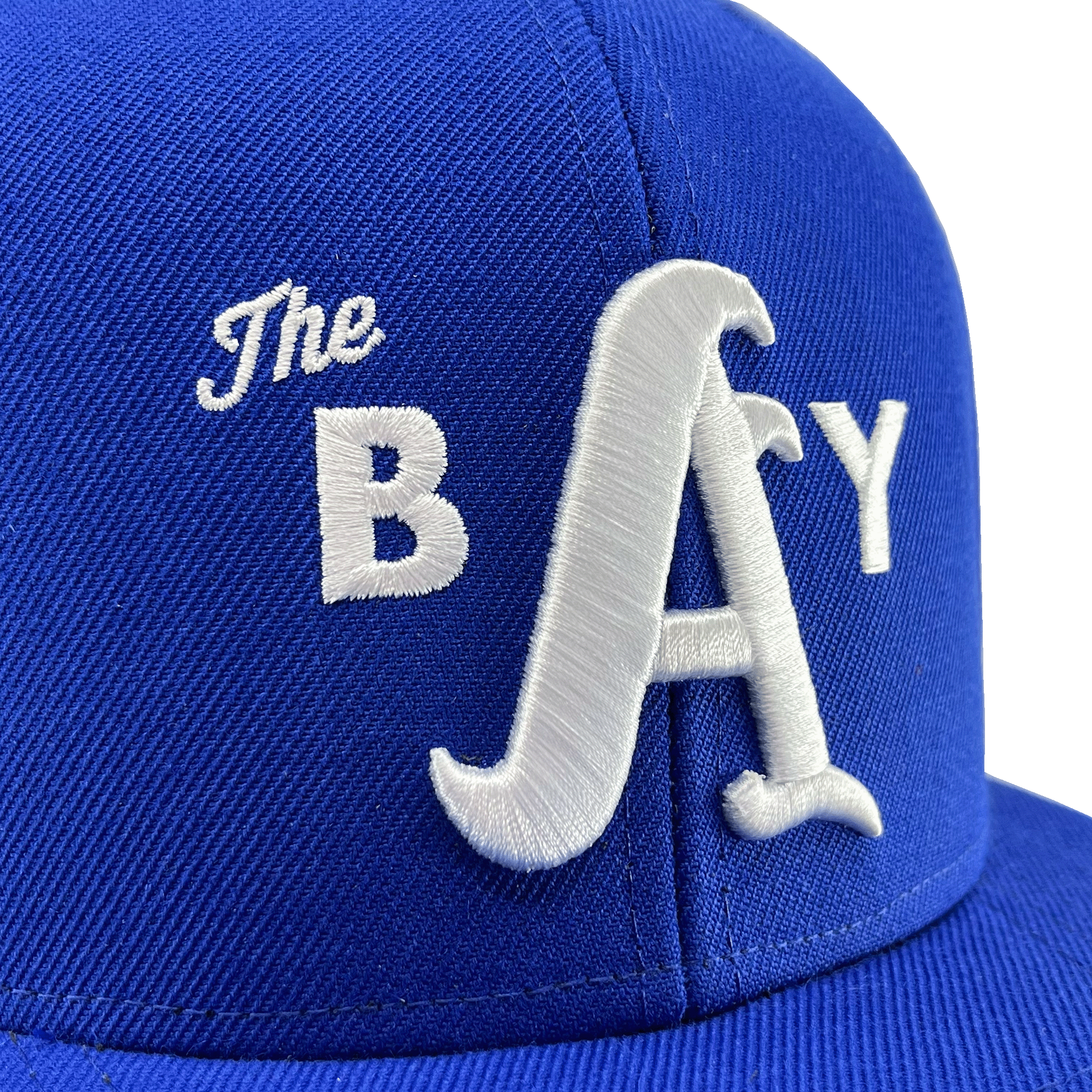 Close-up of a 3D white embroidered The Bay logo on the crown of a royal blue hat.