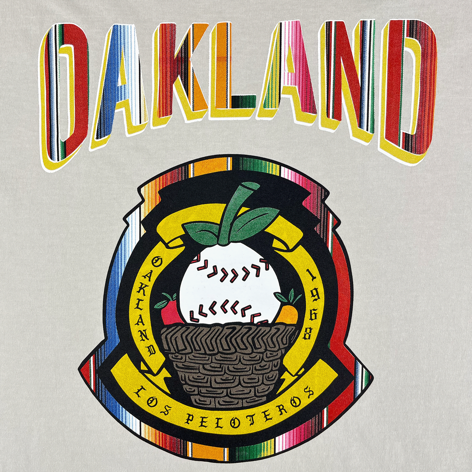 The image shows "OAKLAND" in bold letters above a round emblem with a baseball in a basket, green leaves, and "OAKLAND 1968 LOS PELOTEROS," celebrating the Oakland Ballers and featured on the Oakland Beisbol Heavy Tee.