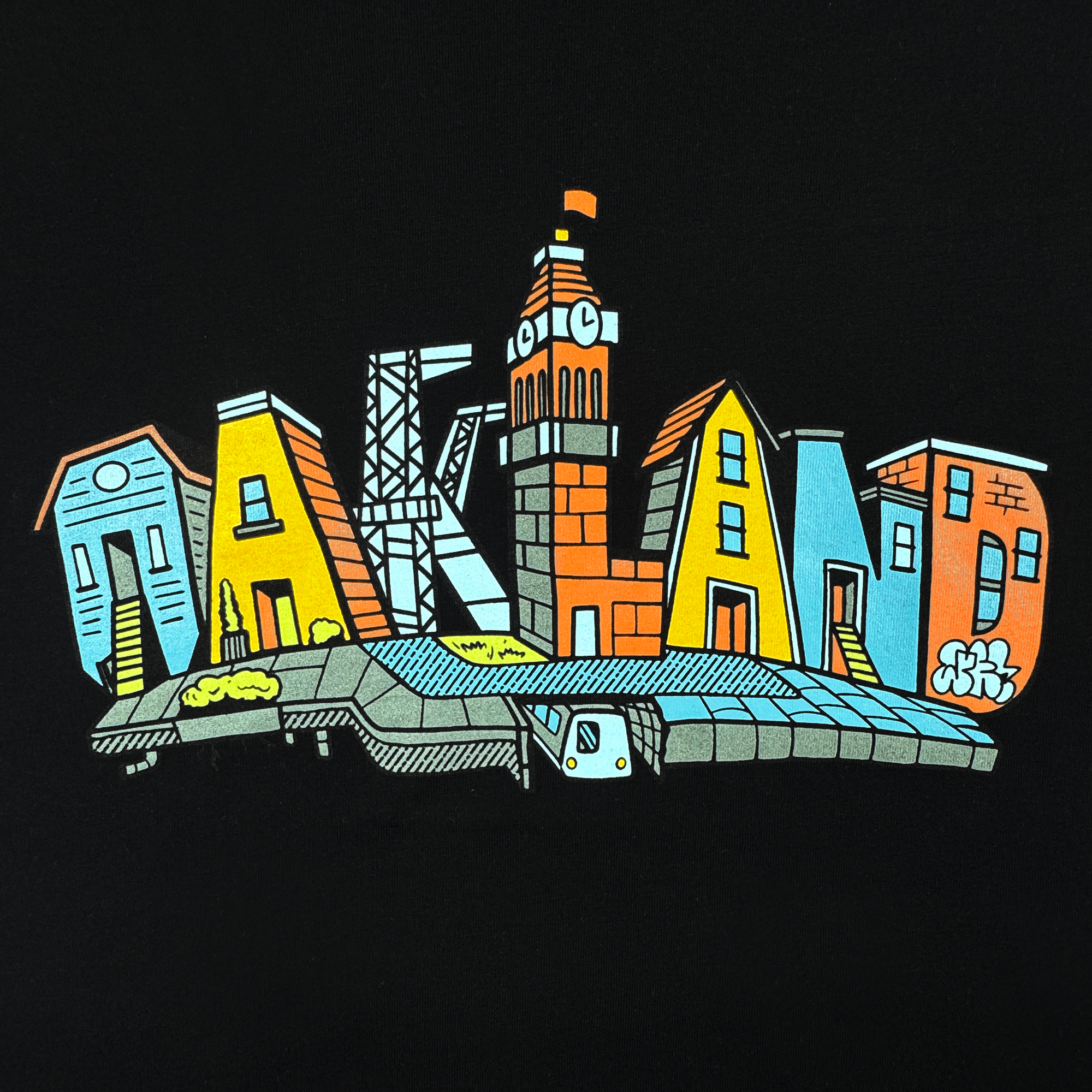 The Oaklandish Toddler Blockletters Tee features “Oakland” spelled out in illustrated buildings, including the clock tower and skyline, with a BART train below and urban touches like trees and graffiti.
