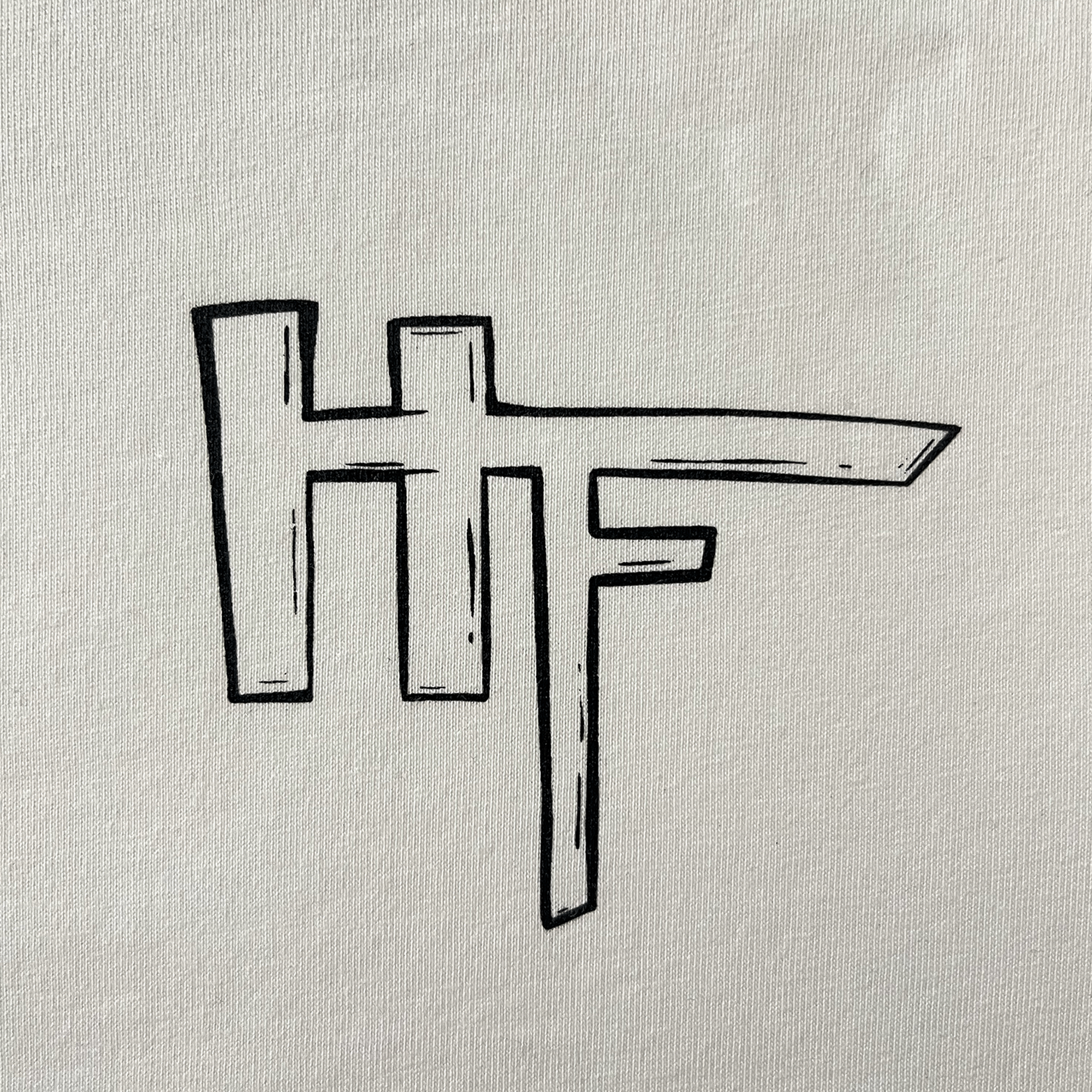 Close up of Oakland artist HellaFutures' signature on the front chest of a natural cotton color t-shirt.