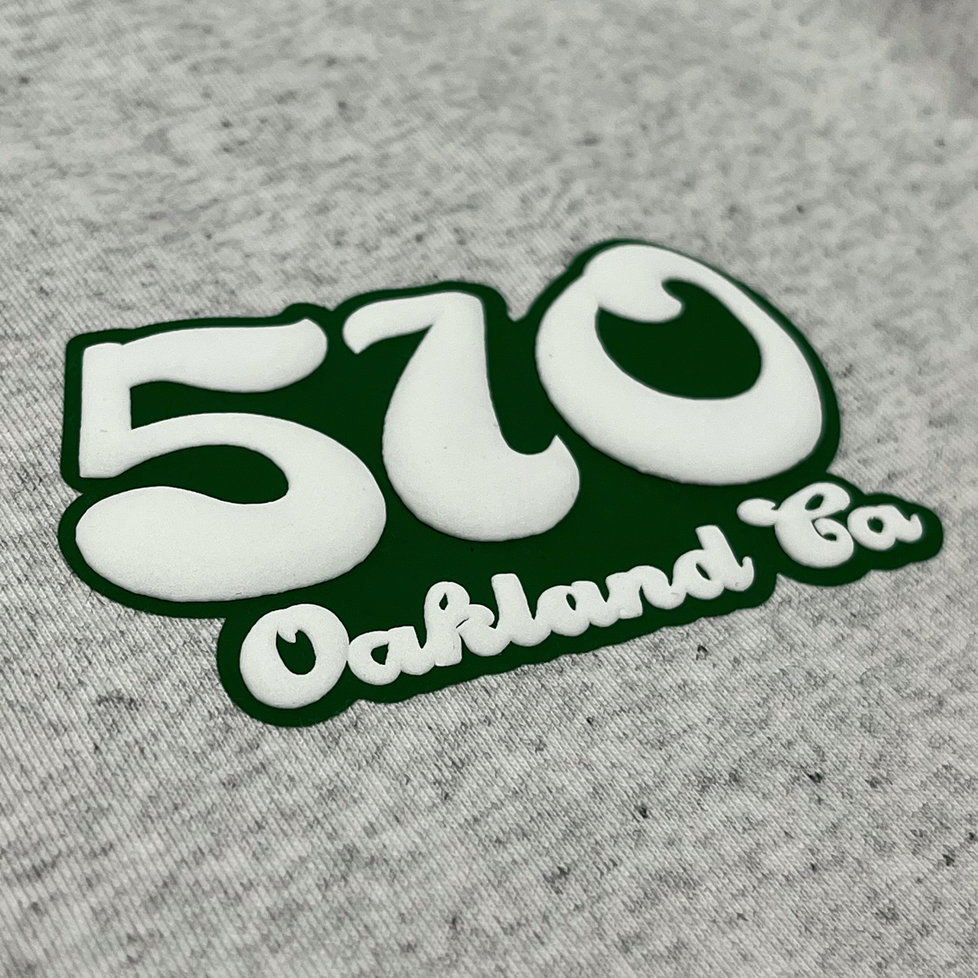 Detailed close-up of puff 510 Oakland CA graphic on left chest wearside of heather grey t-shirt.