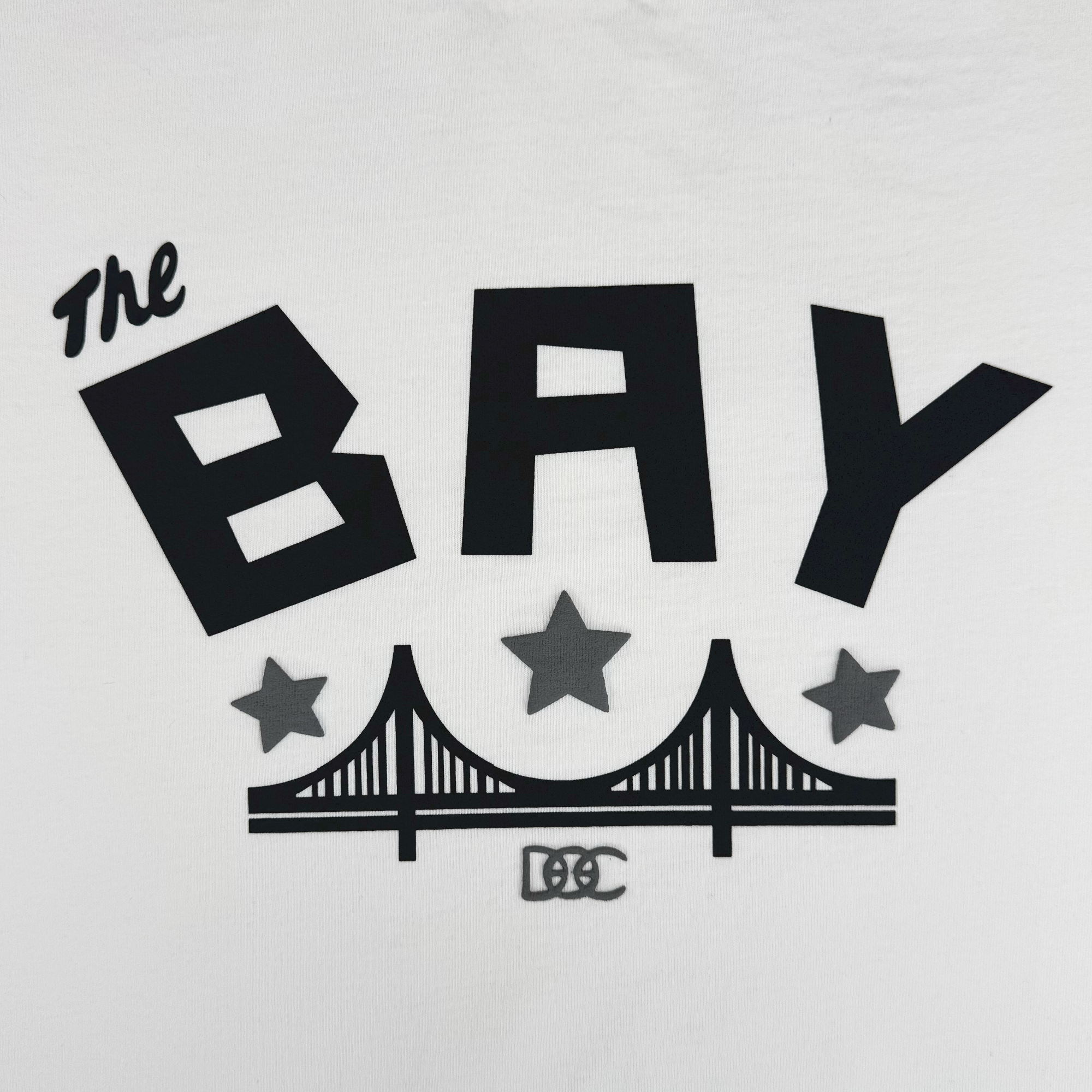 The Bay Bridge Hoodie By DOC V2 from Oaklandish features bold “The BAY” text above a bridge and three stars, with “DOC” below. Part of The Bay Collection, this men's fleece pullover hoodie delivers standout style.