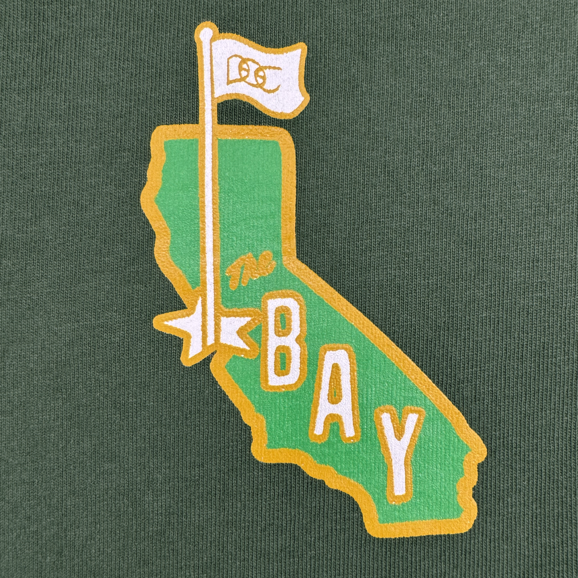 The CA Bay Area Tee By DOC from Oaklandish features a green California silhouette with yellow outline, a white flag marked "OC," a yellow star, and bold "The Bay" text on heavyweight dark green cotton. Part of The Bay Collection.