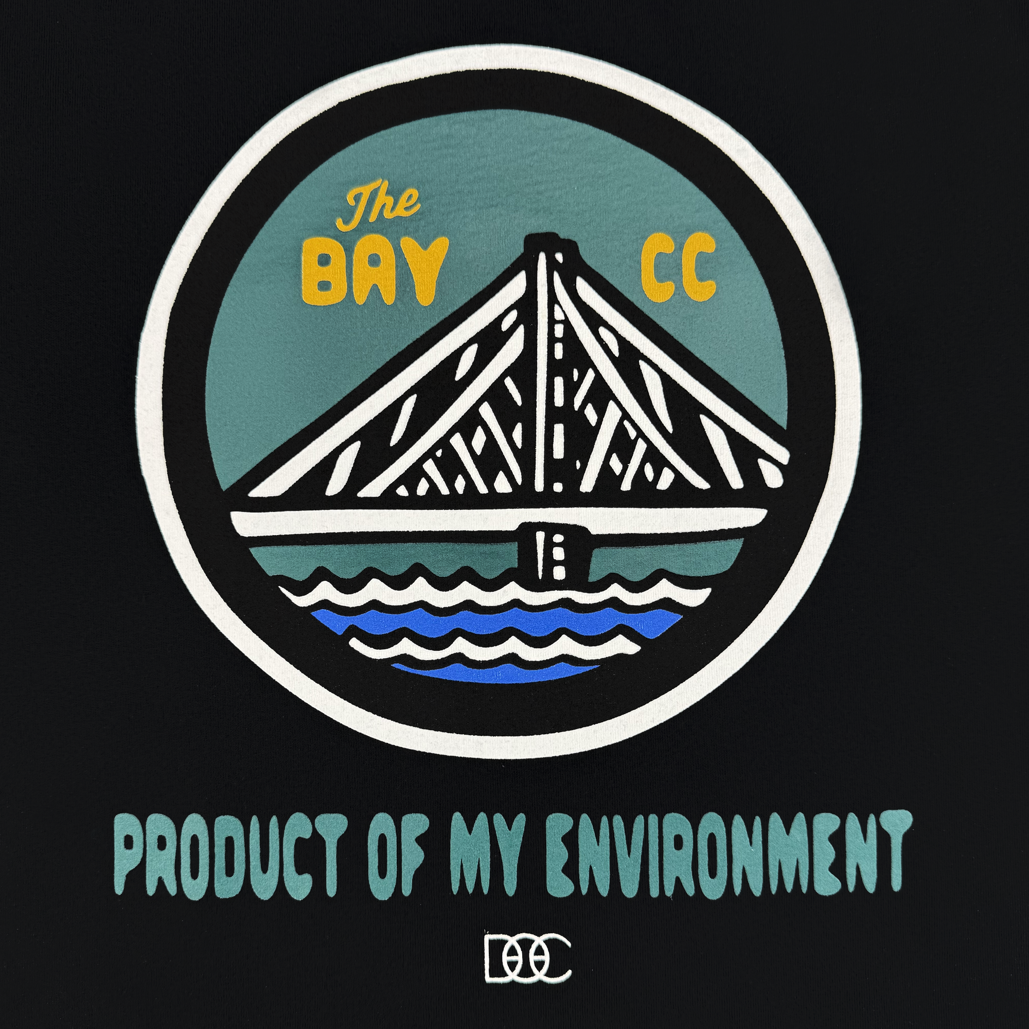 A stylized bridge over water in a circle, “The BAY CC” above, “PRODUCT OF MY ENVIRONMENT” below in teal capitals. Featured on the black Bay Area CC Tee By DOC from Oaklandish’s The Bay Collection, with a white logo at the bottom.