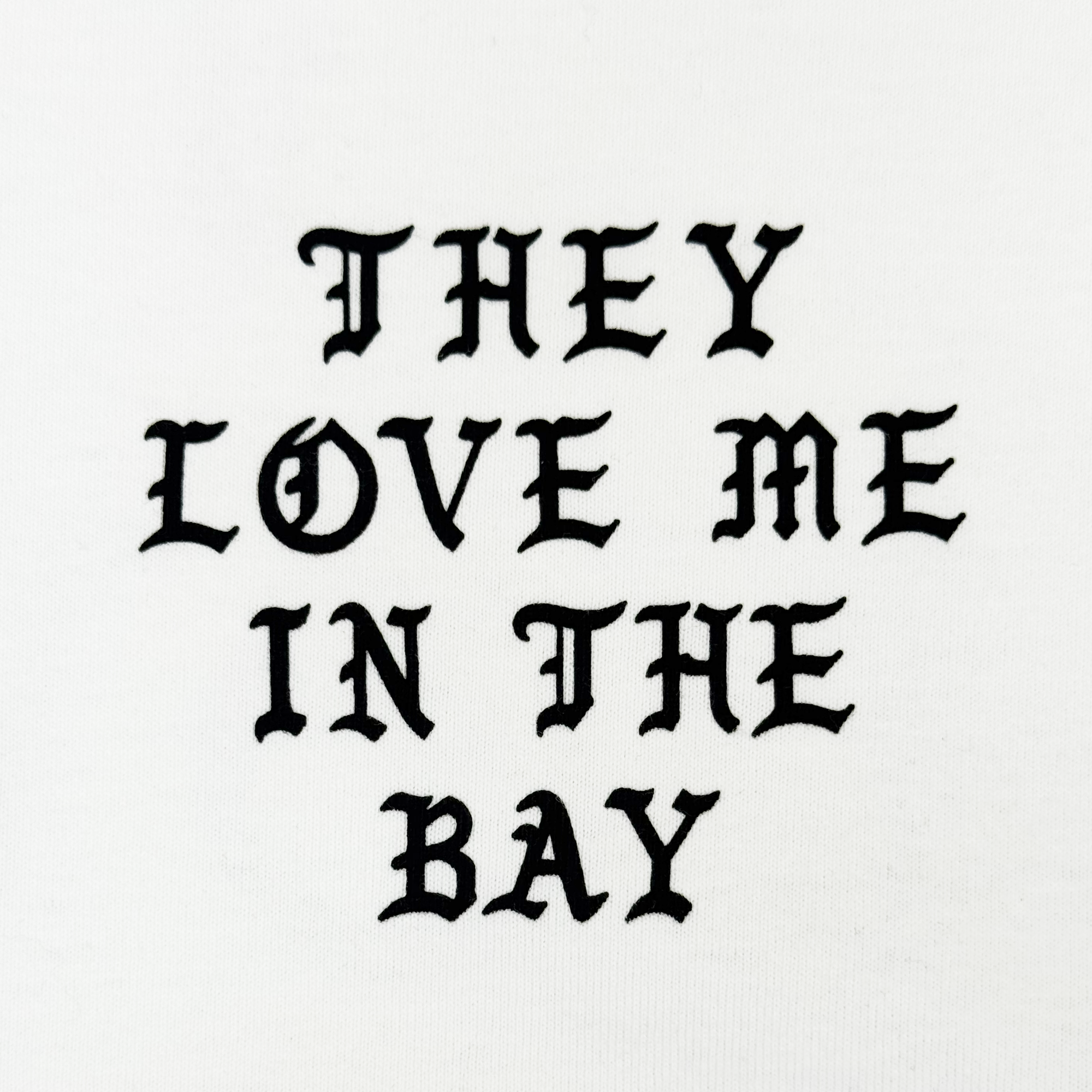 The They Love Me LS Tee By Doc by By DOC features bold, black gothic-style text that reads “THEY LOVE ME IN THE BAY,” centered and evenly spaced across three lines on a crisp white heavyweight cotton long sleeve t-shirt. Designed with men’s sizing, it combines standout style with exceptional comfort.