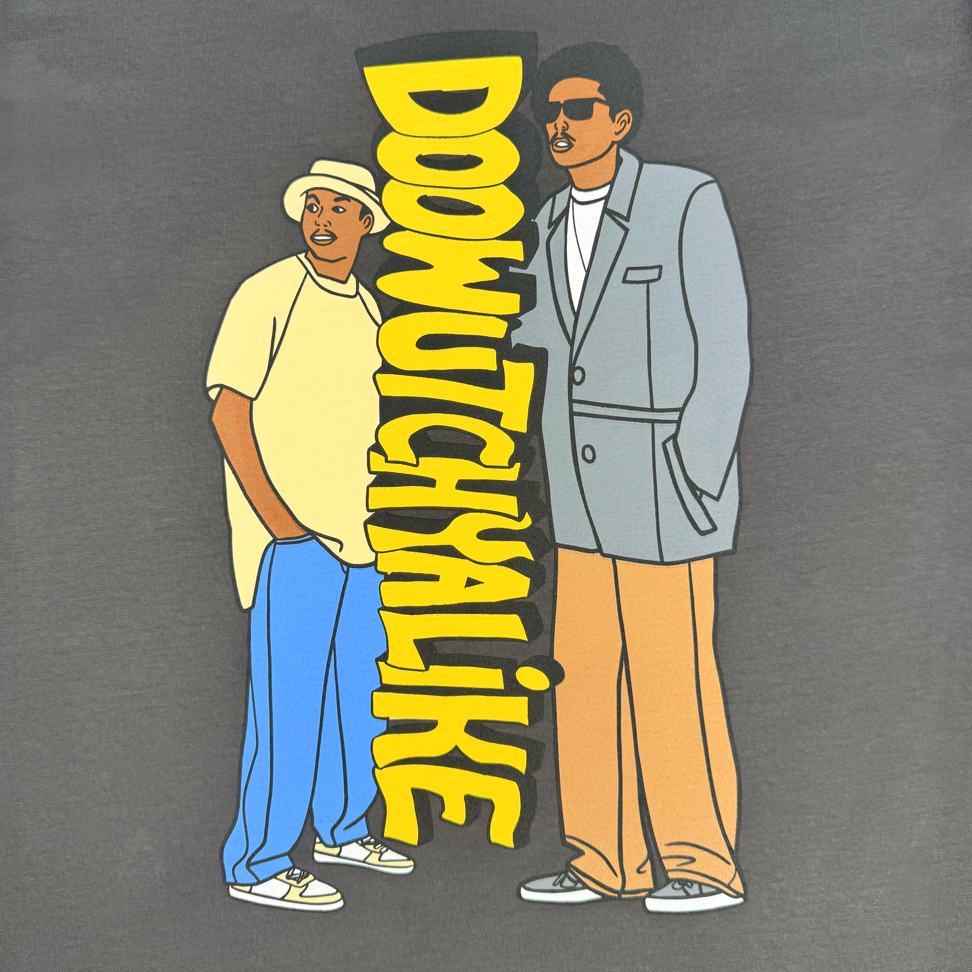 The Oaklandish "Doowutchyalike Tee" features a vibrant cartoon-style of two men, one in a casual hat, t-shirt, and jeans and the other in a gray suit with sunglasses. The bold yellow "DOOWUTCHYALIKE" captures 90s vibes against the dark background, echoing Digital Underground style.