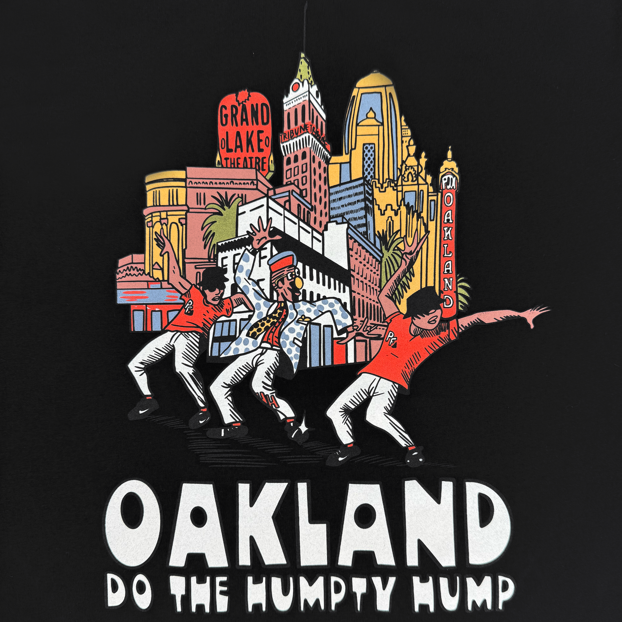 The Do the Humpty Hump Tee by Oaklandish features three dancers captured mid-move, showcasing hip-hop flair in colorful clothing and hats. Vivid Oakland landmarks like the Grand Lake Theatre and an iconic marquee are in the background, with "OAKLAND DO THE HUMPTY HUMP" boldly displayed below.