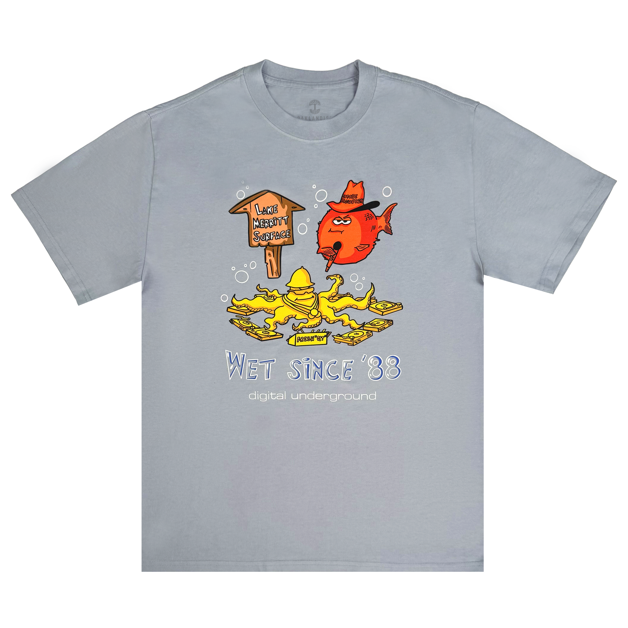 The Oaklandish Wet Since '88 Heavy Tee features a cartoon of a red fish and yellow character underwater near a sign reading "Lake Wabbit Swamp." The text "Wet Since '88" and "Digital Underground" highlights its Oakland roots, with bubbles adding to the aquatic feel.