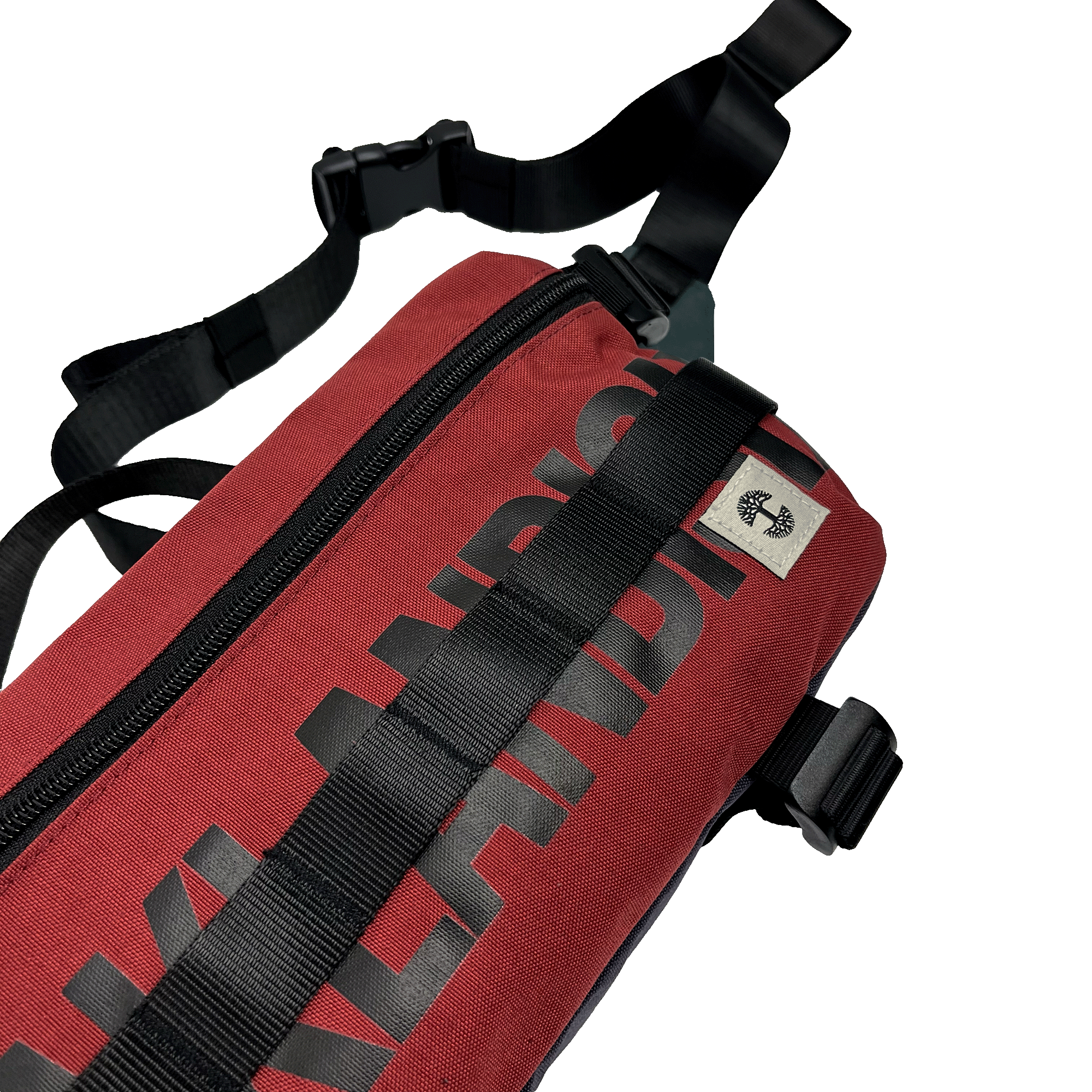 A close-up image of the Oaklandish Hip Bag, a red shoulder bag featuring black straps and a black zipper. The word "Oaklandish" is printed in bold black letters along the side of the bag. With its unisex appeal and premium details, including a small cream tag with the Oaklandish logo near the top, this versatile bag is positioned on a white background.