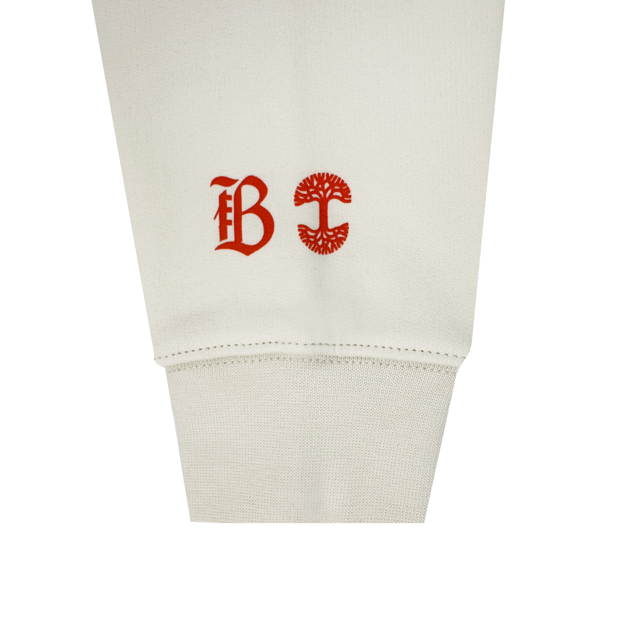A close-up of the Bay FC Jubilee Crew shows its off-white cuff and sleeve, featuring two red symbols: Bay FC’s stylized “B” logo and a circular tree emblem, printed side by side above the cuff.