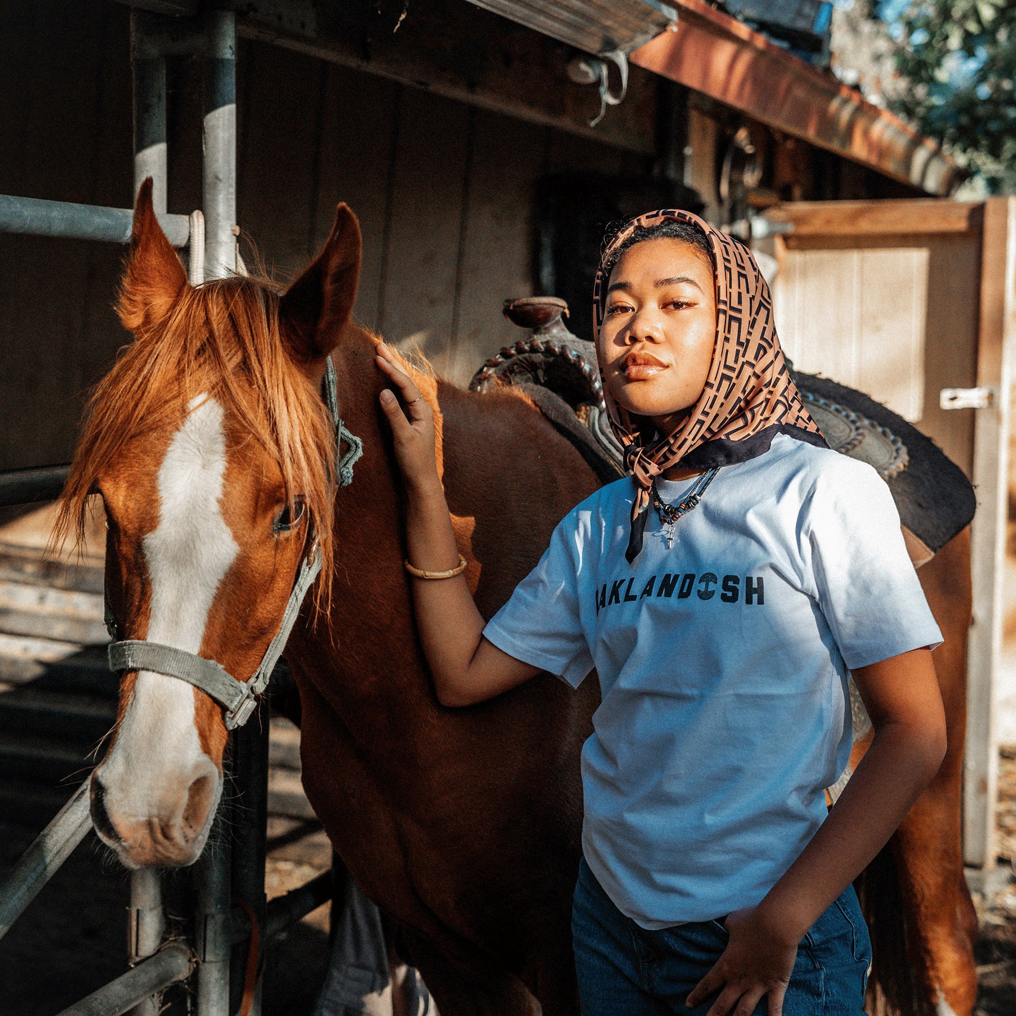 Model with horse wearing cotton white t-shirt with Oaklandish Wordmark and Oaklandish tree logo in place of 'i'.