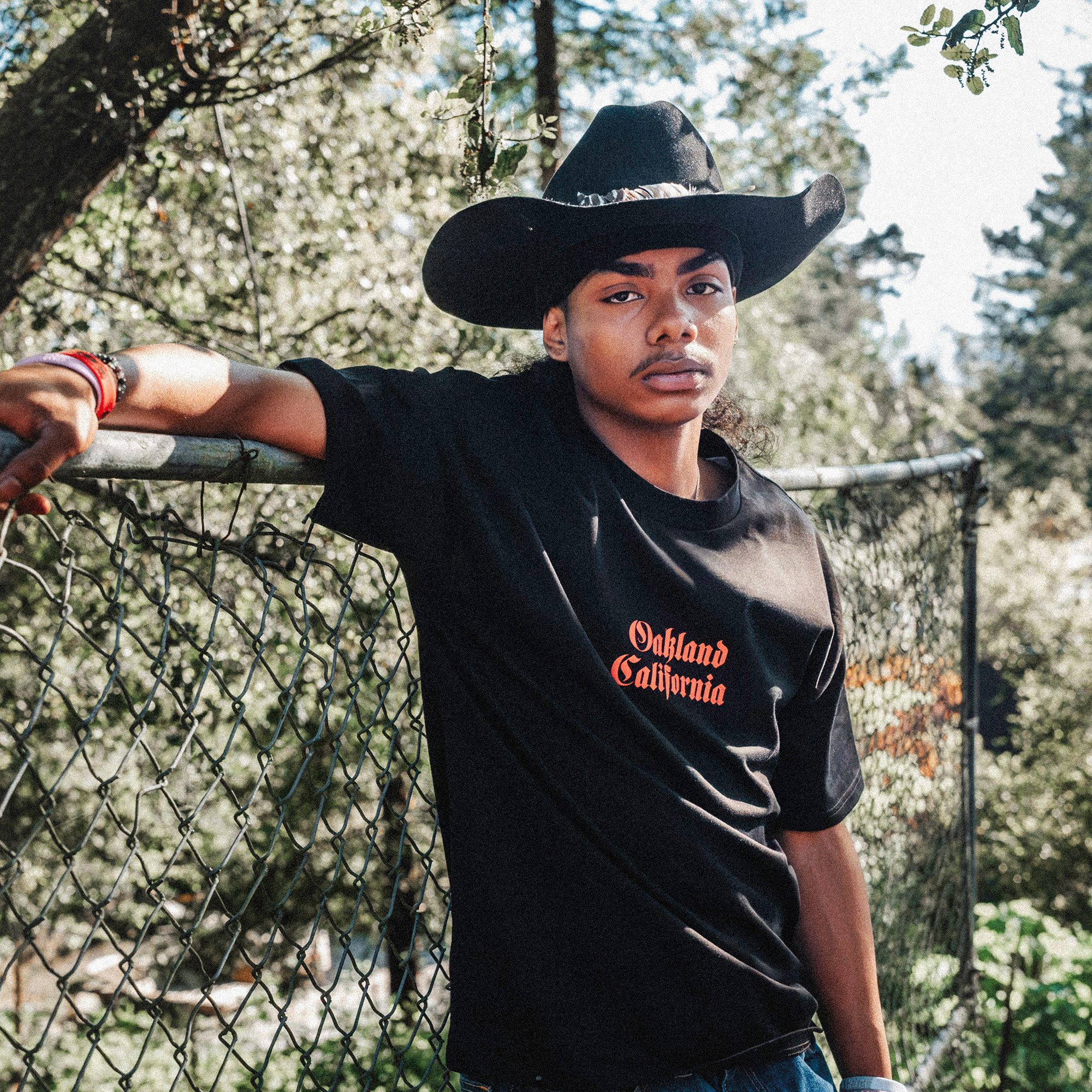 Front view of model wearing black tee with Oakland California printed center in red ink.