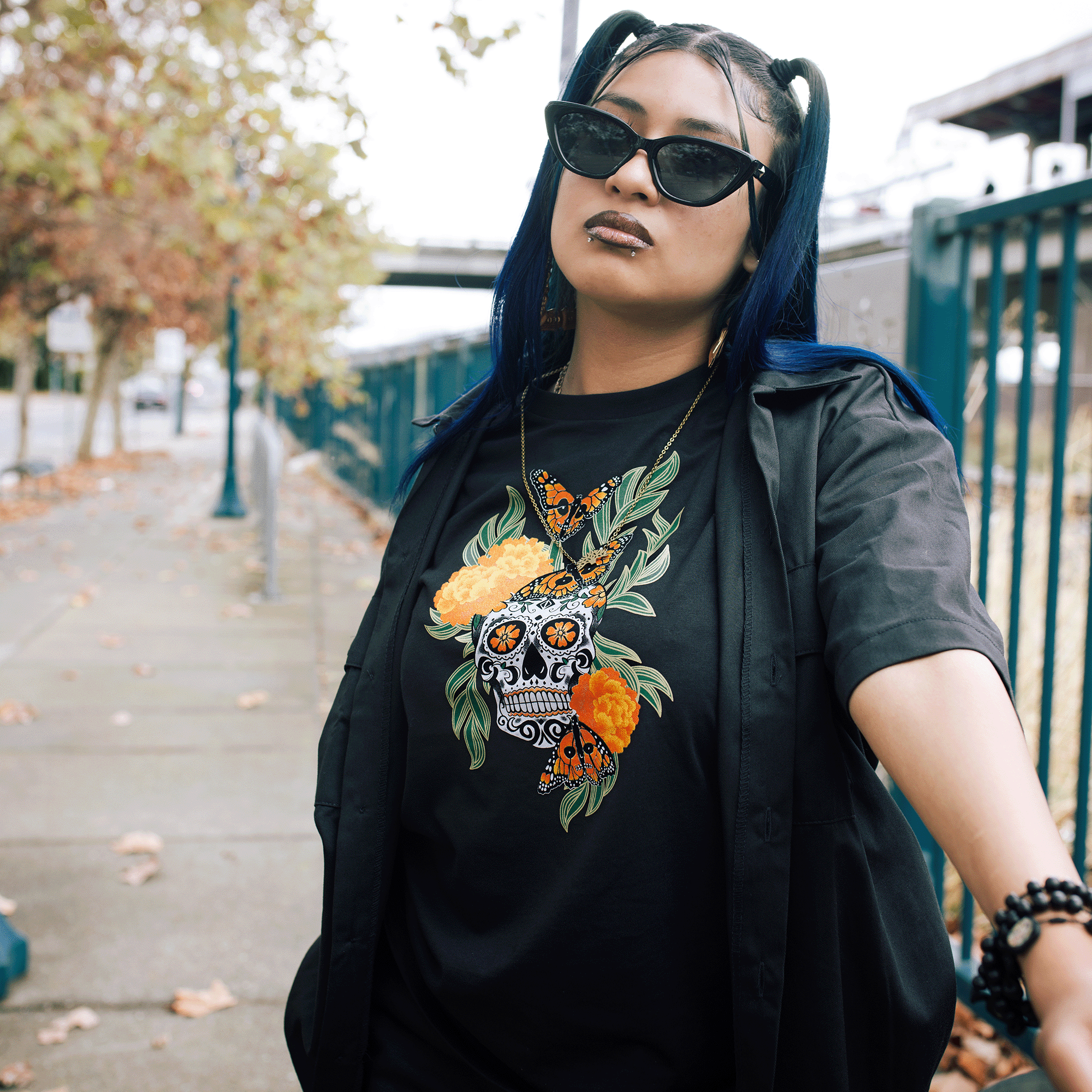 Female model wearing black t-shirt with graphic art by Oakland artist Jet Martinez depicting a sugar skull surrounded by Marigolds and Monarch butterflies with over shirt.