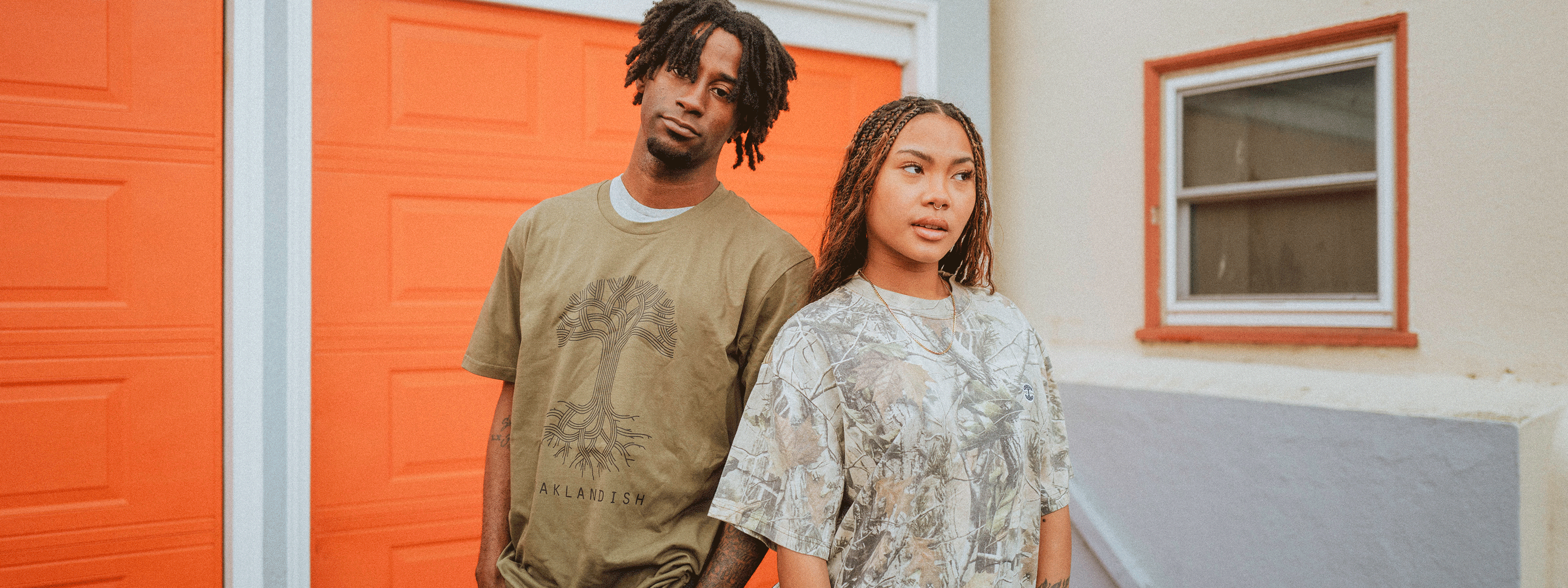 male and female standing outside of a house wearing Oaklandish t-shirts