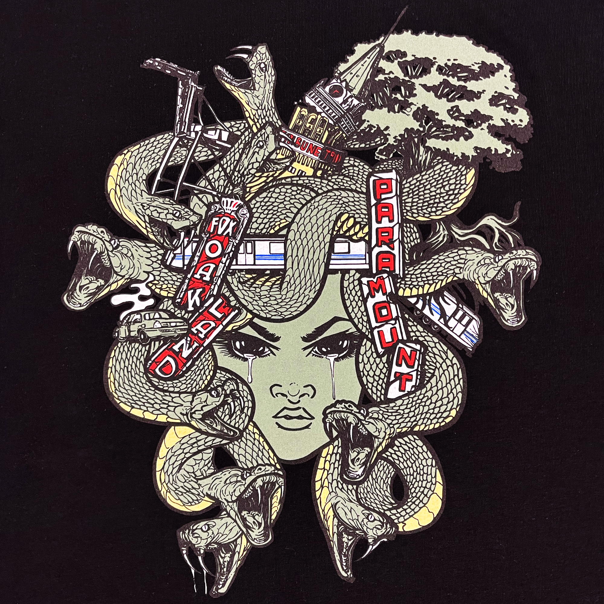 Introducing the **Medusa Tee by Oaklandish**: This classic fit t-shirt features a striking graphic of a stylized female face with multiple snakes emerging from her head, reminiscent of Medusa. Surrounding her are iconic landmarks such as a tree, bridge, and signs reading "FOX", "OAKLAND", and "PARAMOUNT". The design is brought to life with bold colors and intricate details set against a dark background.