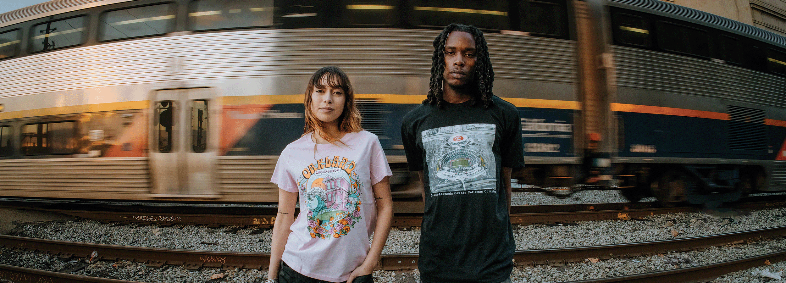 Models wearing Oakland Dream and Mems tees in front of a moving train.