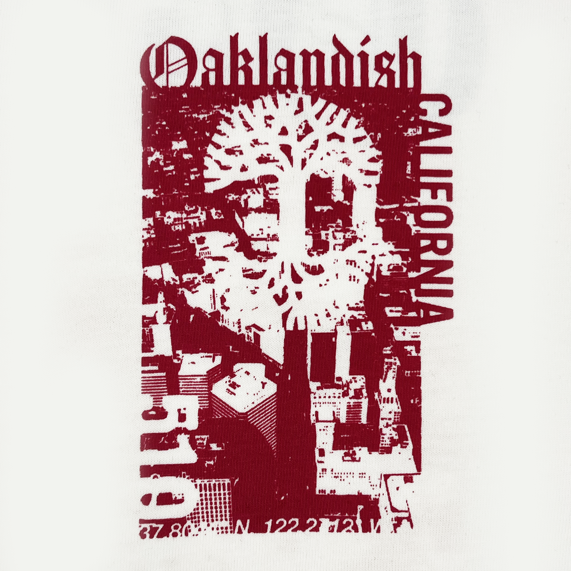 Close-up of abstract red Oaklandish graphic on the left chest of a natural cotton-colored t-shirt.