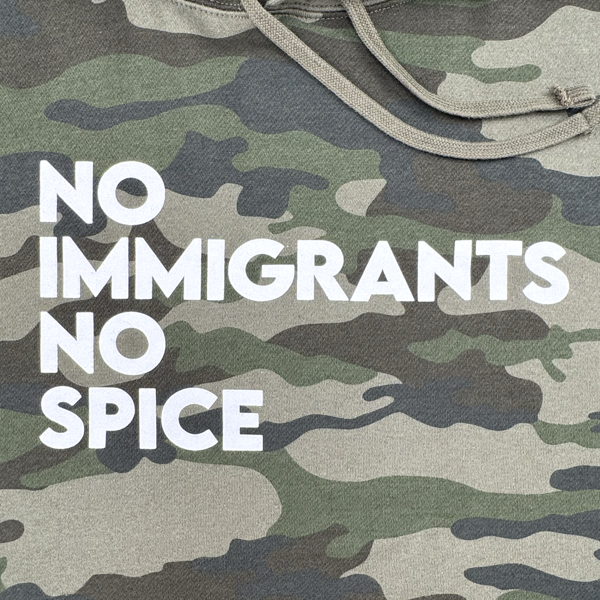 The Oaklandish NINS Hoodie features a camouflage pattern with bold white "NO IMMIGRANTS NO SPICE" text on the left side, partially covered by a drawstring, celebrating immigrant rights and spicy pride.